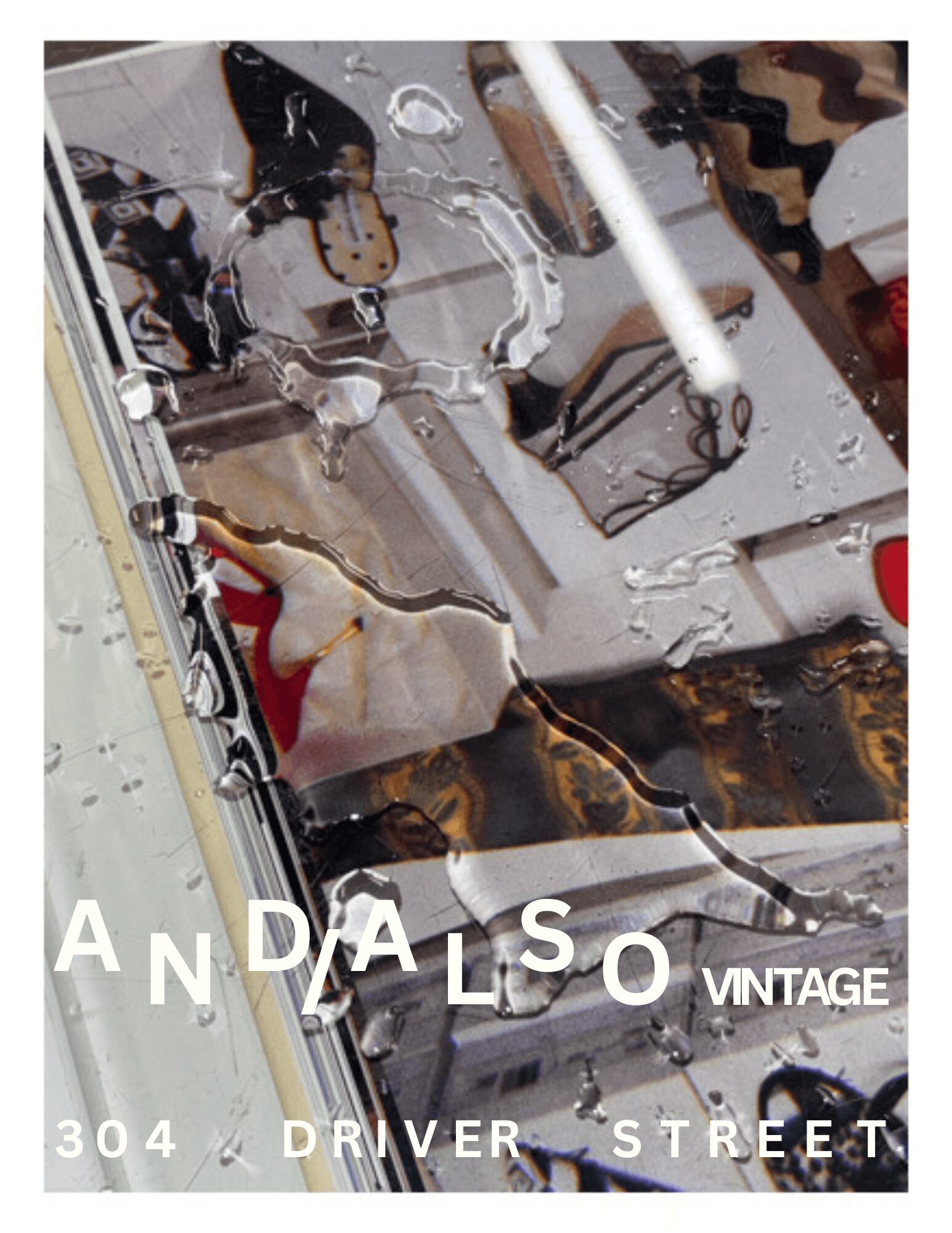 Reflected image of a vintage car with text 'ANDALSO VINTAGE 304 DRIVER STREET' on a wet surface.