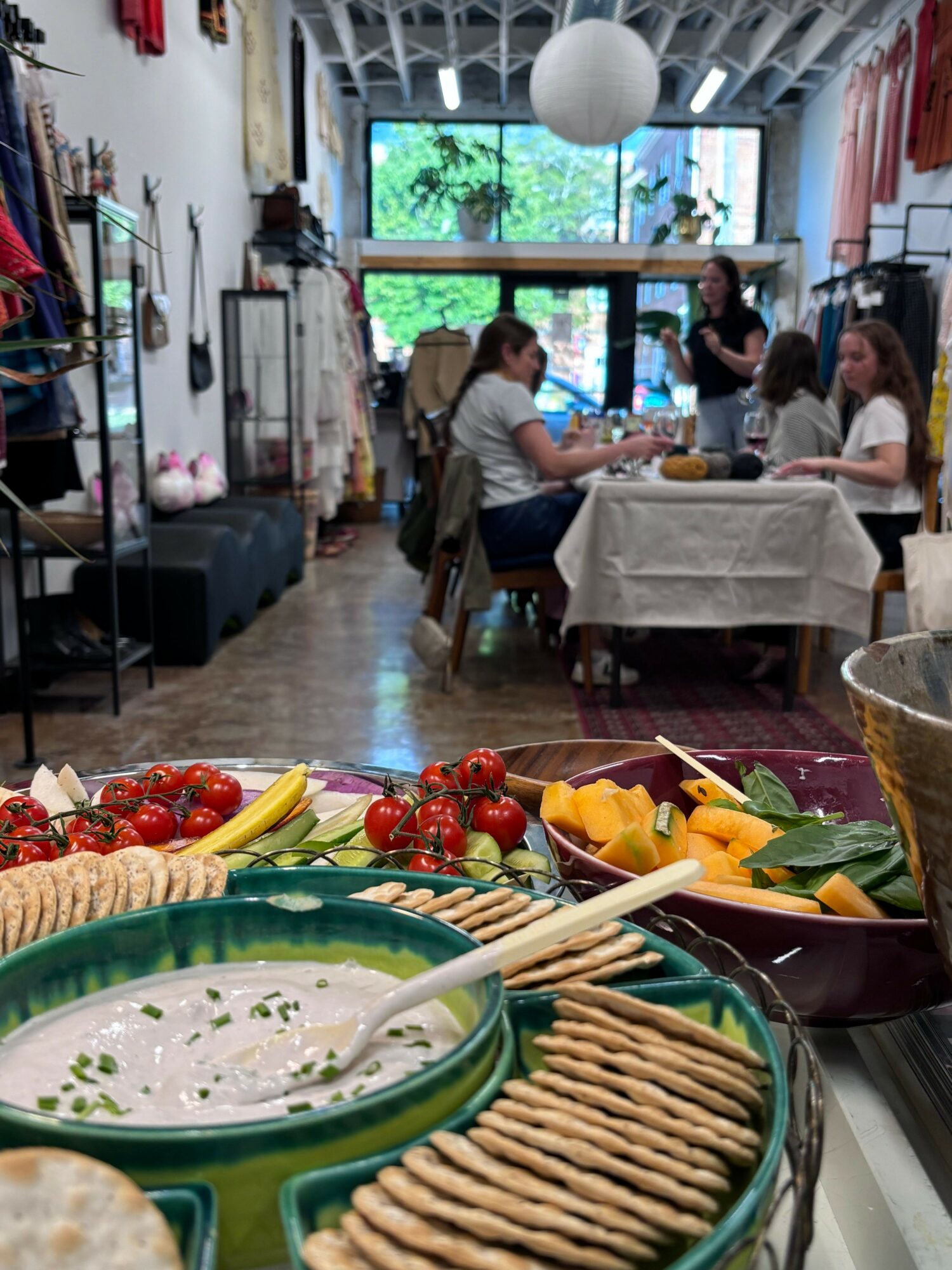 People gathered around a dining table with food, drinks, and a window view in the background.