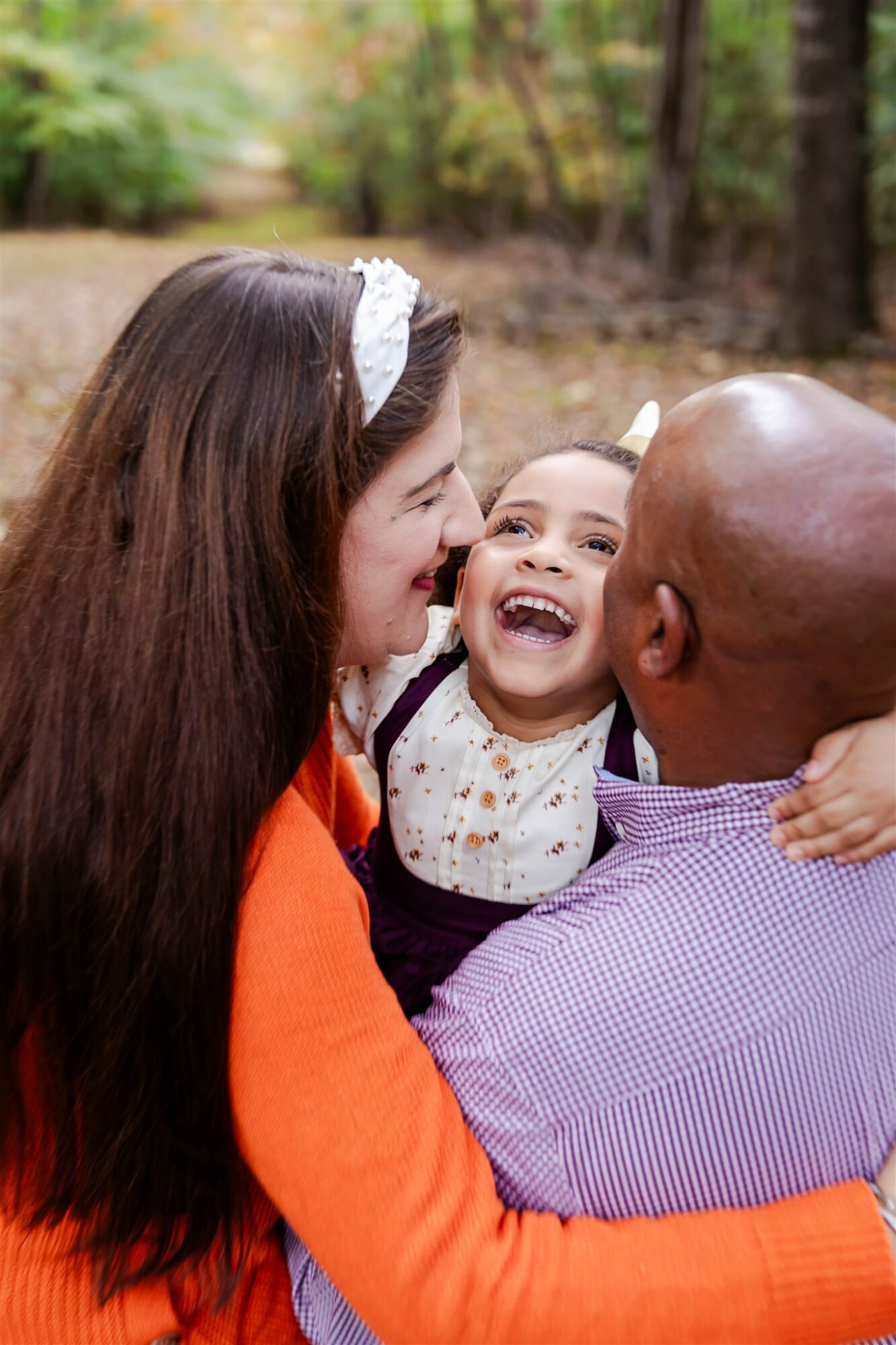 Family of three smiling and embracing outdoors in a wooded area.