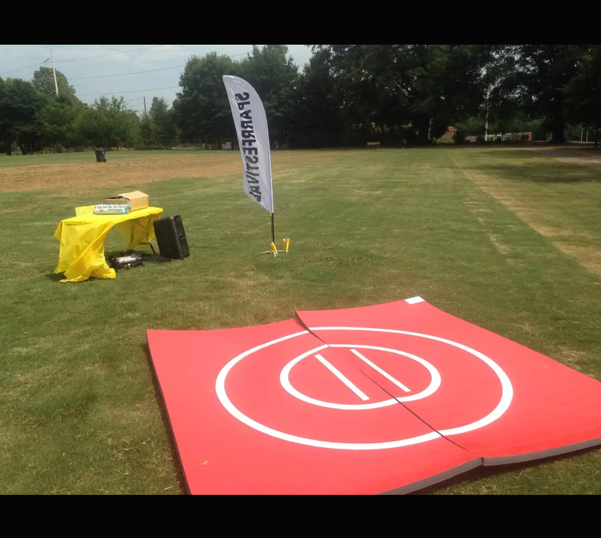 Golf practice area with a red mat, flag, and yellow equipment on grass field, trees in background.
