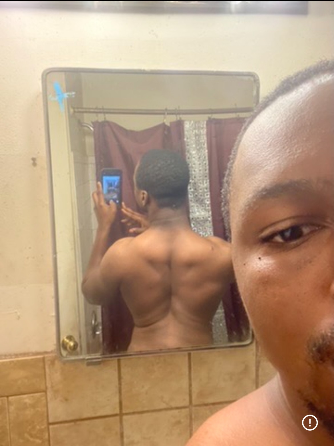 Person taking a shirtless mirror selfie showing back muscles, with part of their face visible in the foreground.