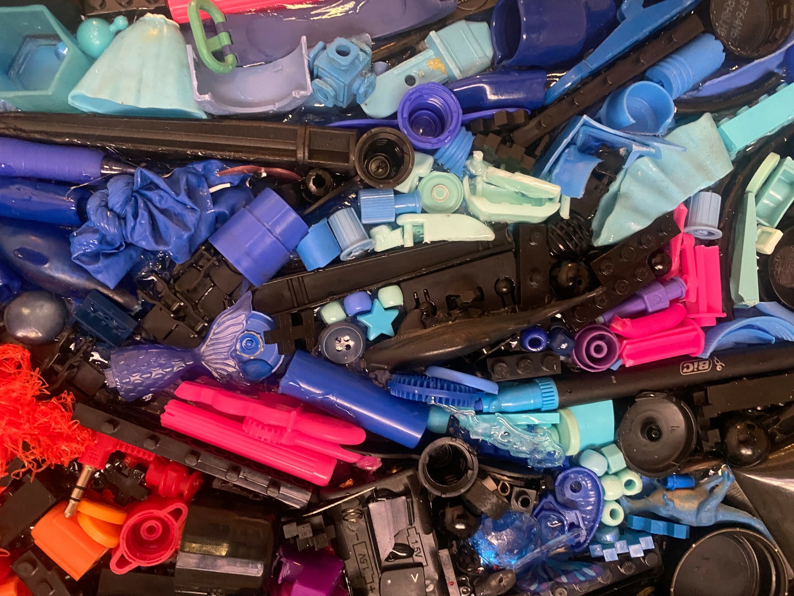 A pile of colorful plastic and rubber objects, including tubes, caps, and small parts, in various colors and sizes.