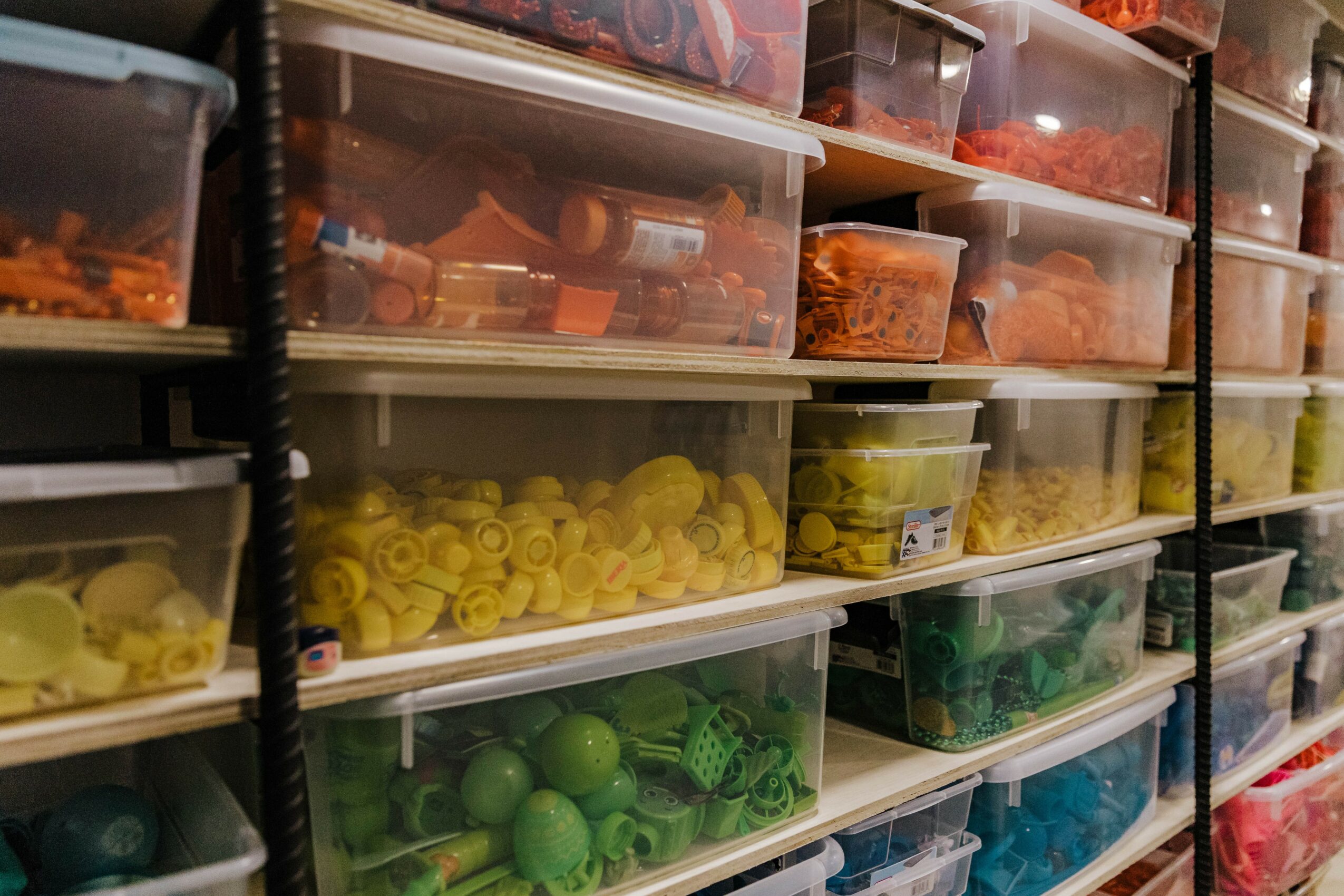 Multiple transparent plastic storage bins filled with colorful plastic toy parts arranged on shelves.
