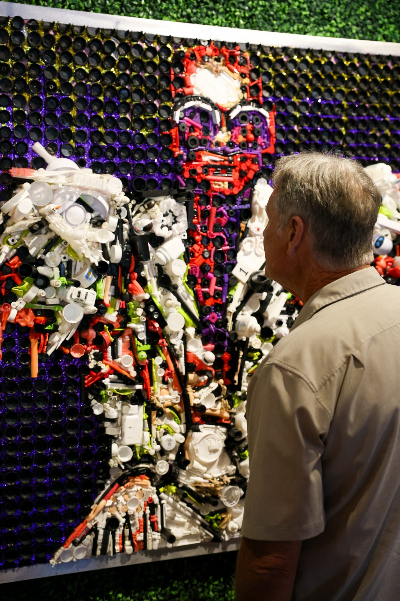 Man observing a colorful robot sculpture made of LEGO bricks against a black background with yellow accents.