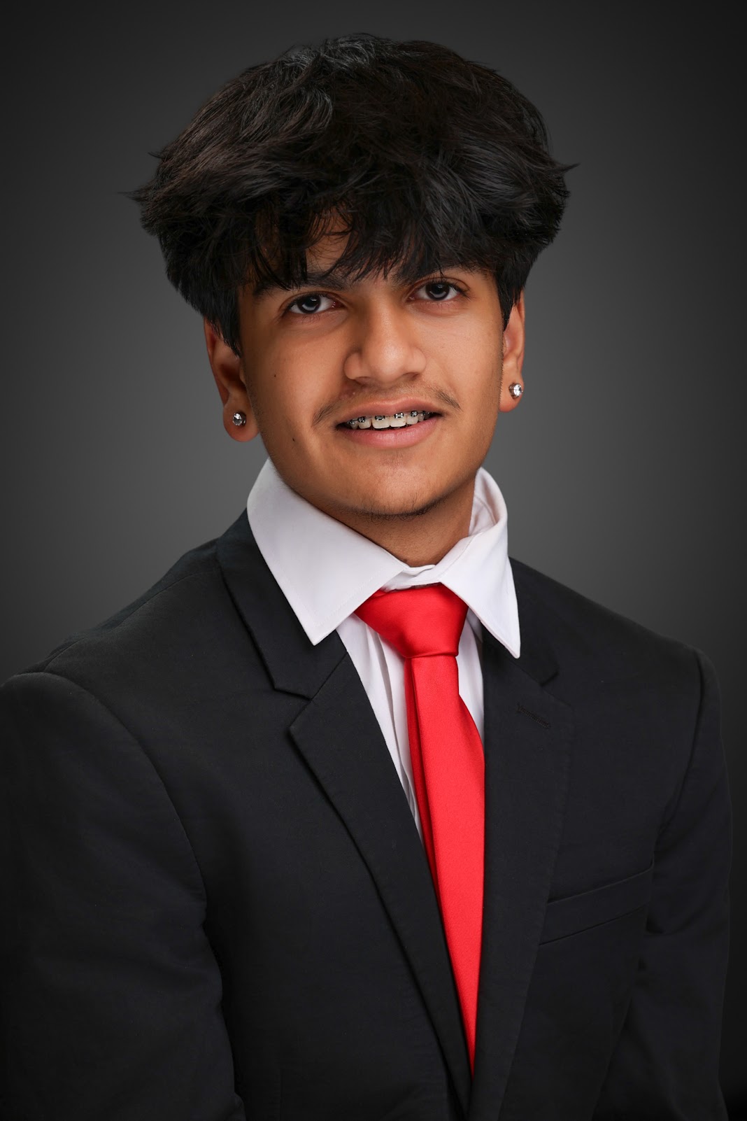 Young man in formal suit with red tie, smiling, against dark background.