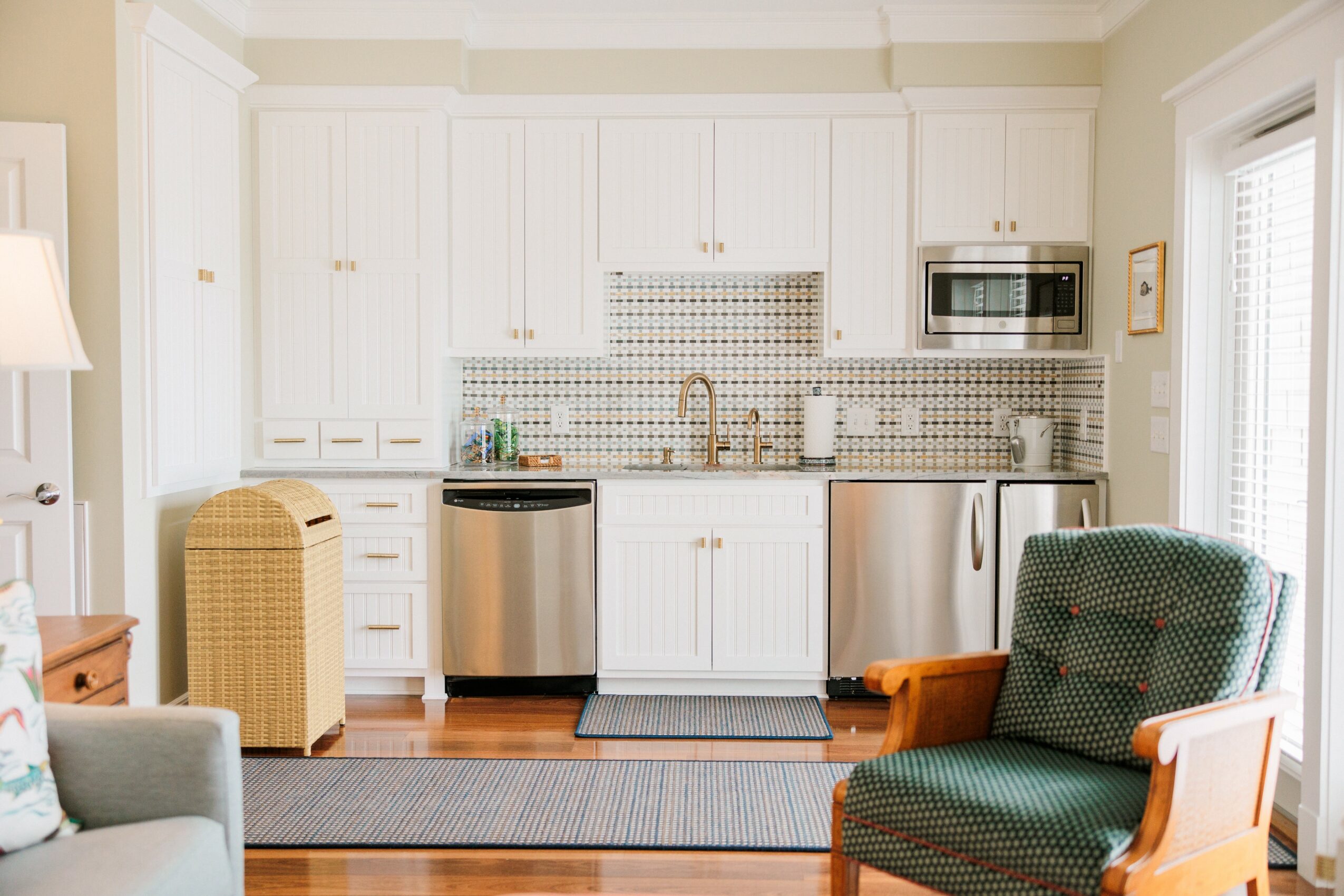 Kitchen with white cabinets, stainless steel appliances, and a patterned backsplash. Two chairs are visible, one green and one wicker.