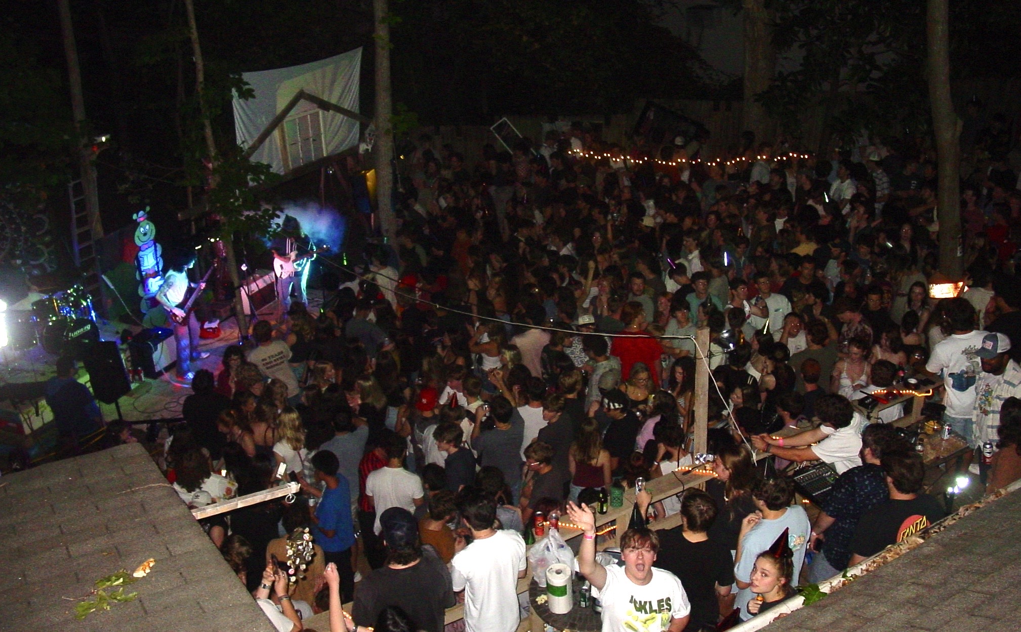 Crowd gathered at night for a live outdoor concert with stage lighting and performers, viewed from above.