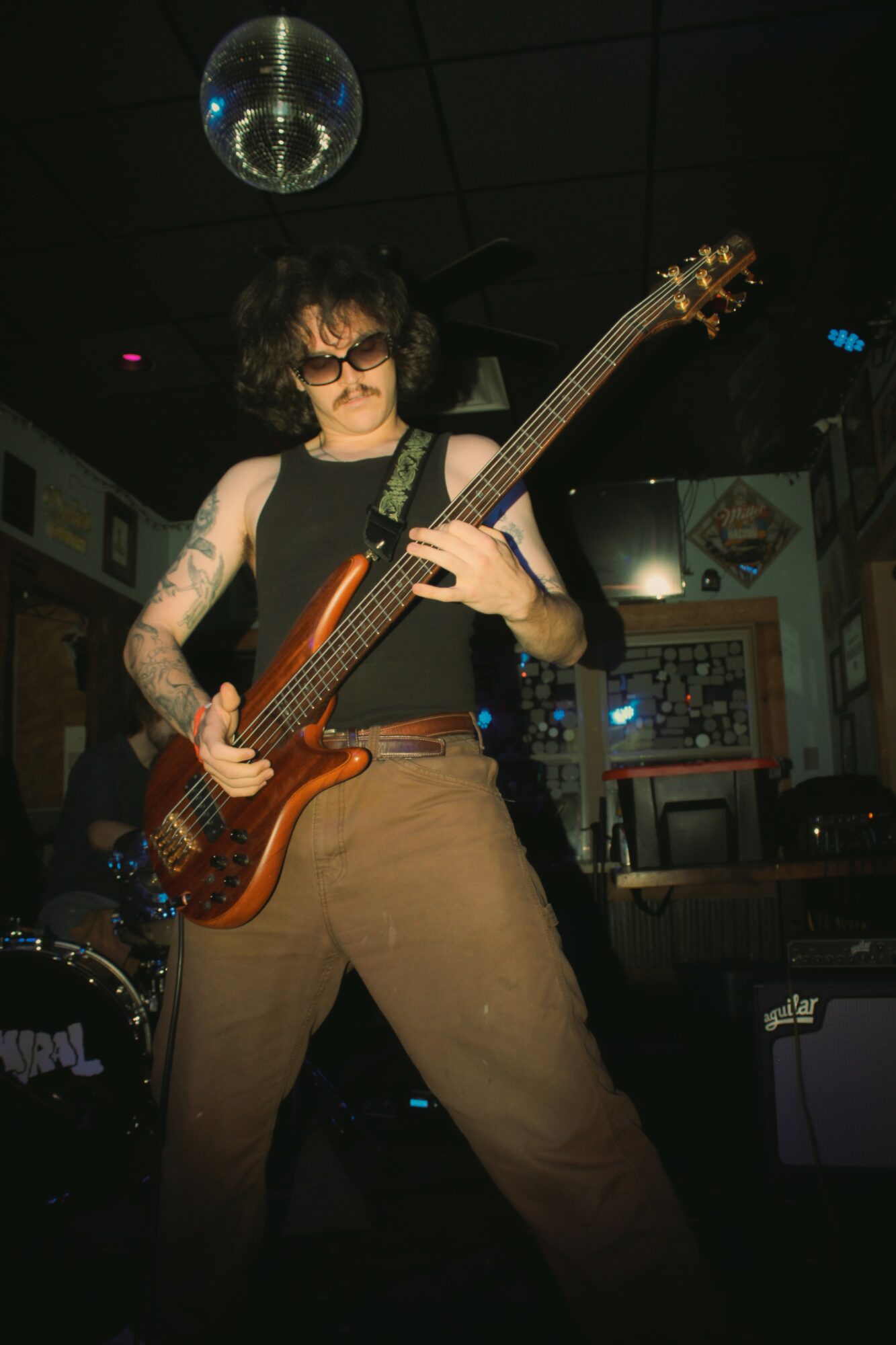 Person playing bass guitar in a dimly lit room with a disco ball overhead.