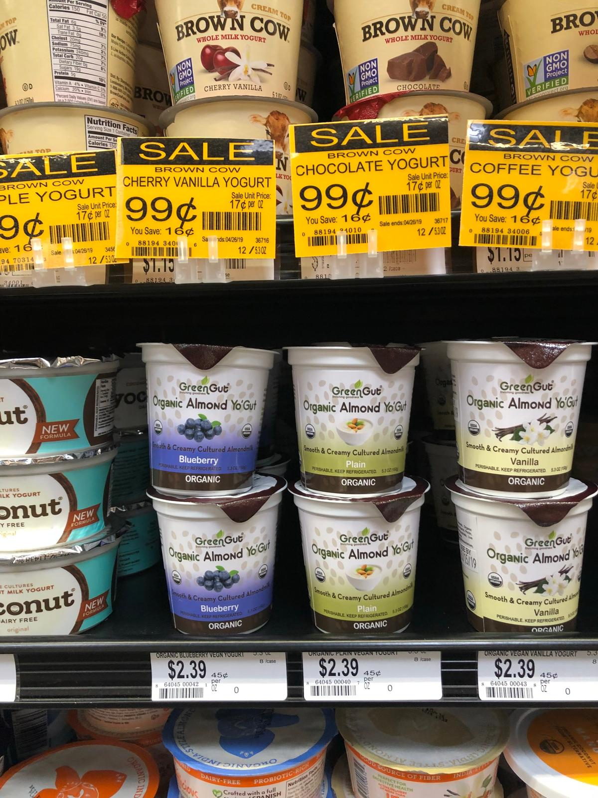 Yogurt containers on shelves with sale tags, priced at $0.99 and $2.39, with various flavors and brands visible.