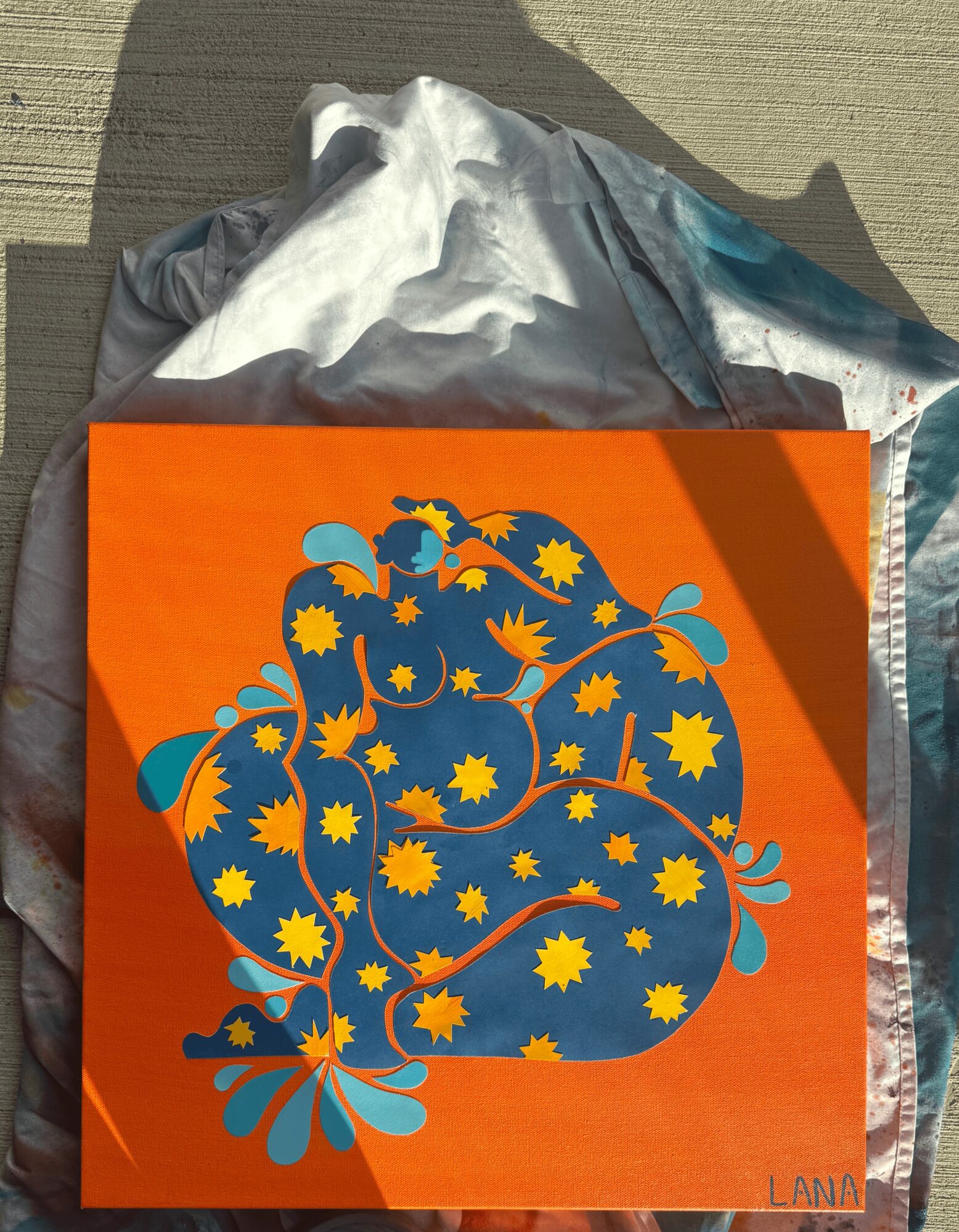 Orange card with a blue floral design and yellow star-like shapes, signed 'LANA' in bottom right corner.
