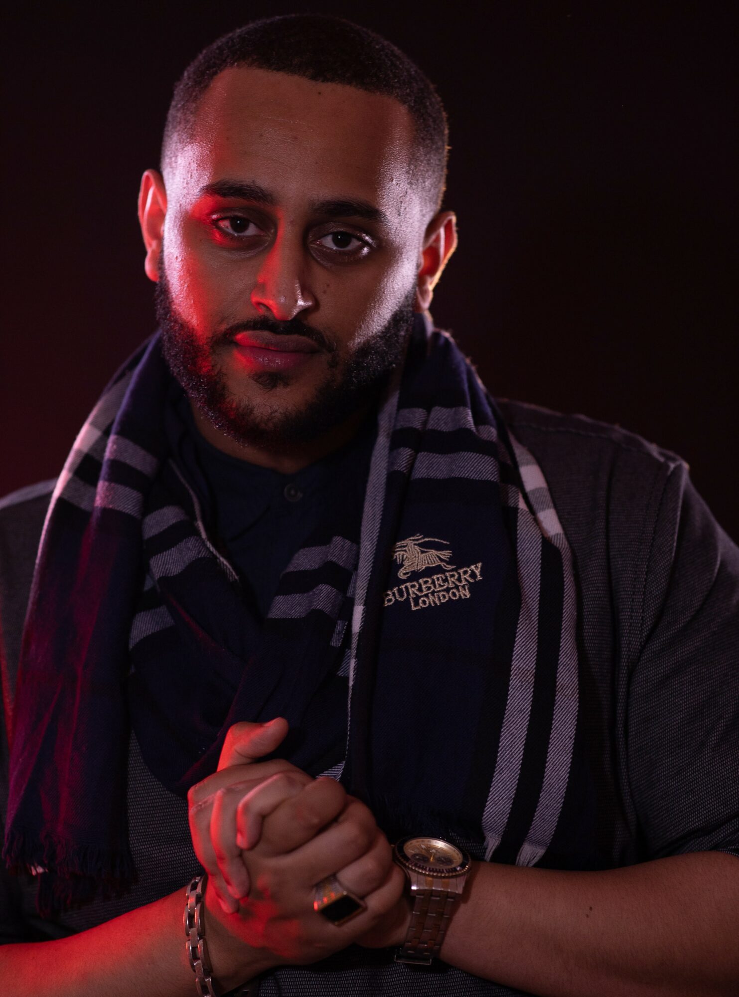 Man with short hair and beard wearing a dark jacket and striped scarf, looking at camera with a serious expression.
