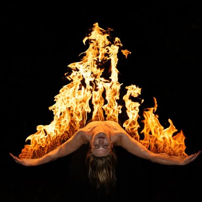 Person lying upside down with arms outstretched, flames behind them, against a black background.