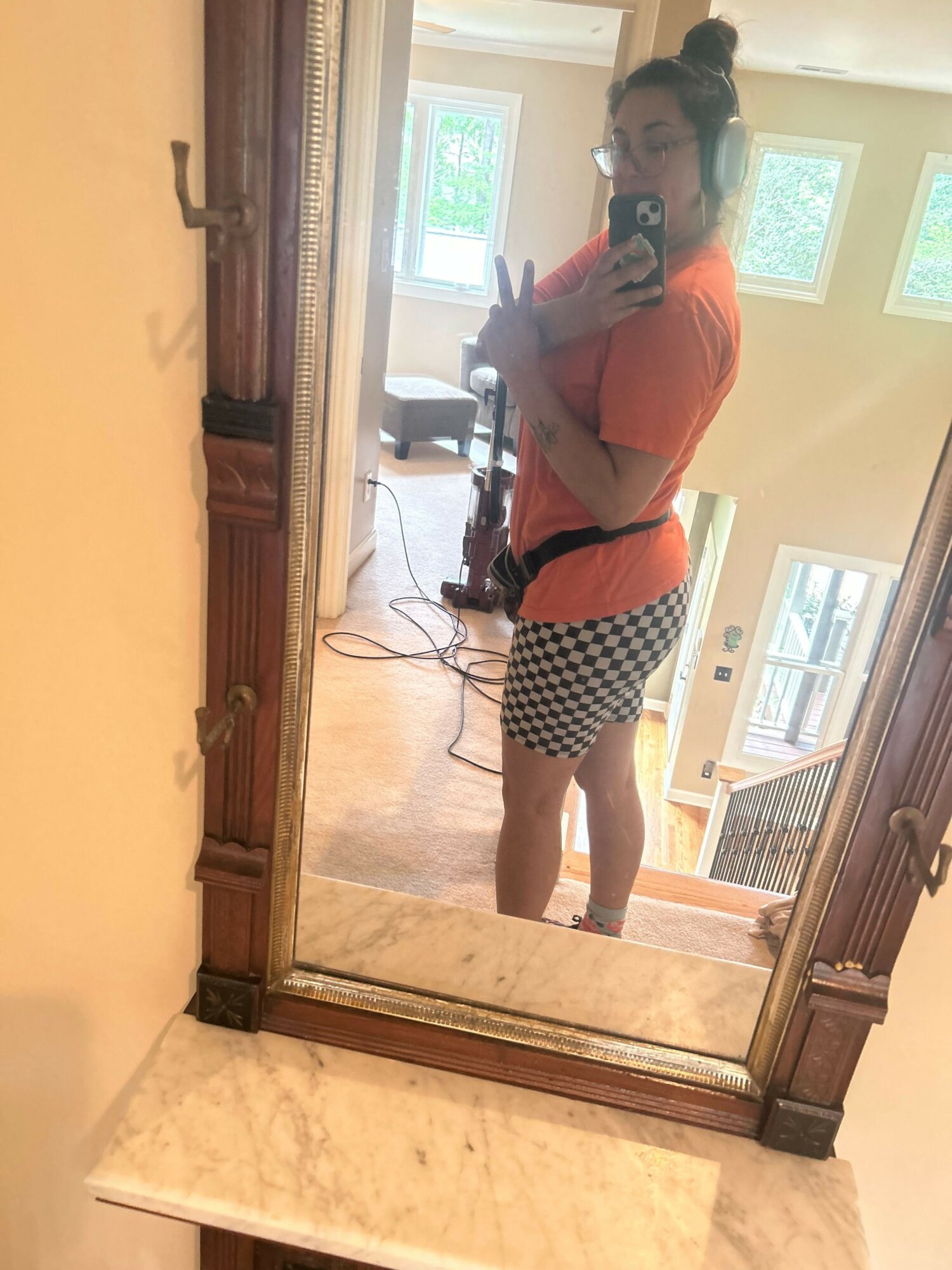 Person taking a mirror selfie in a room with windows, wearing a red top and checkered skirt.