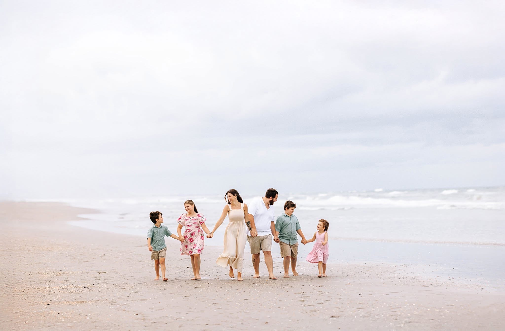 Group of six people, including children, walking on a beach with ocean waves and cloudy sky in background.