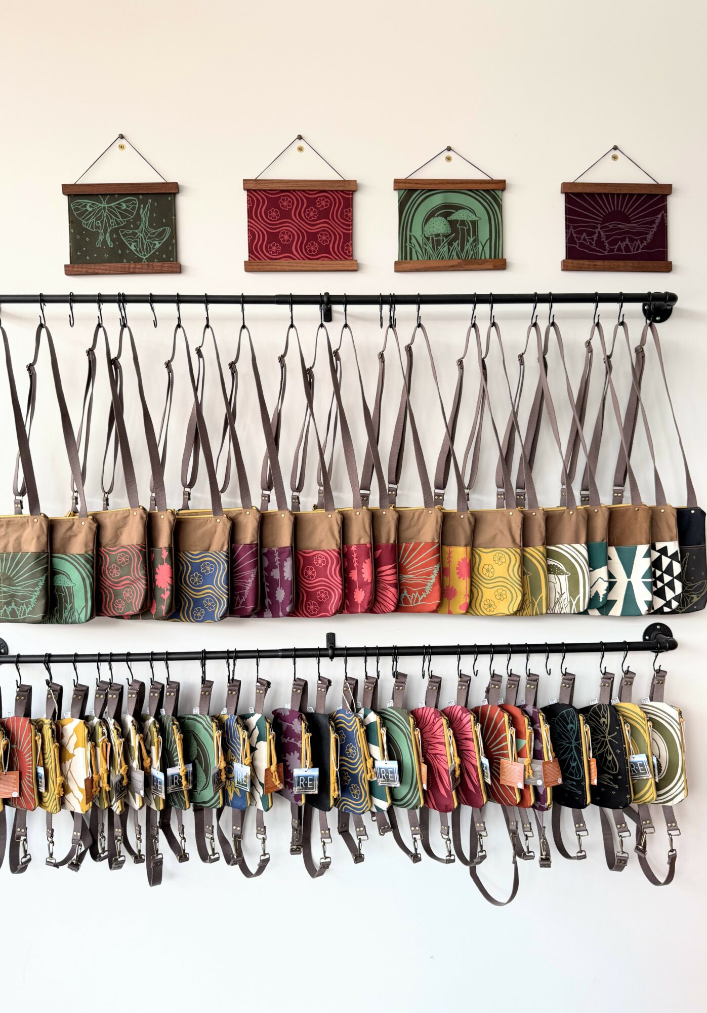 Wall display with hanging fabric samples and small decorative wall hangings above, organized on horizontal rods.