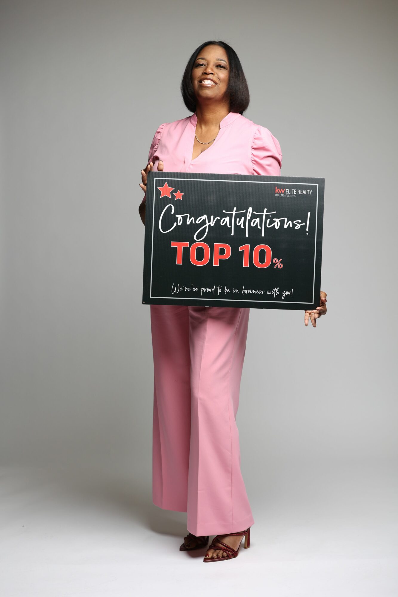 Woman in pink outfit holding a sign with text, standing against a plain gray background.