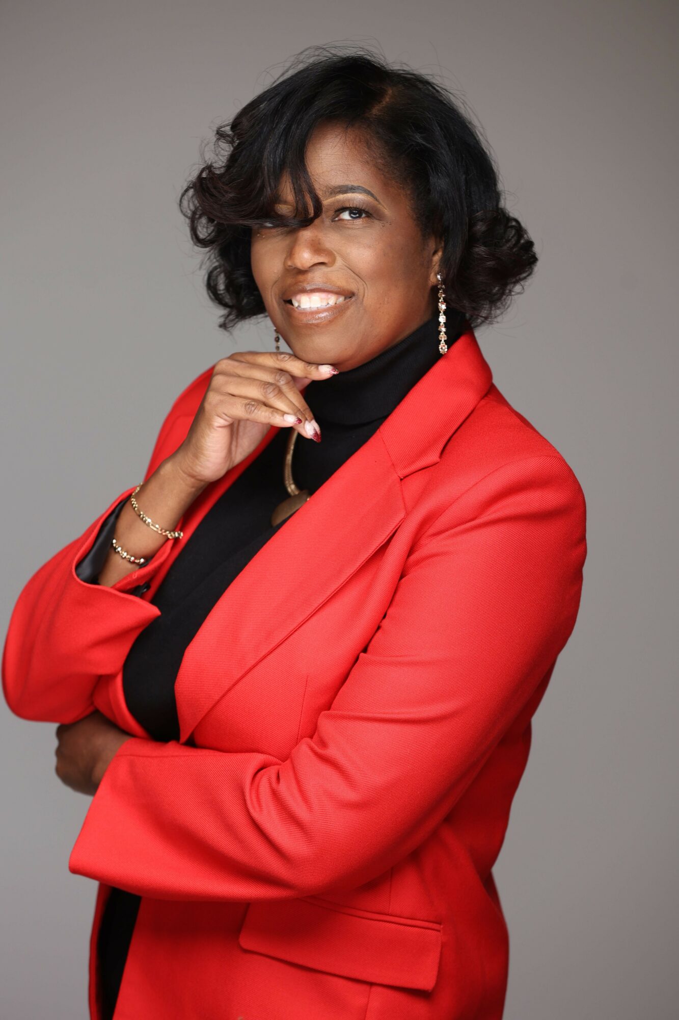 Woman in red blazer smiling, with arms crossed, against a plain background.