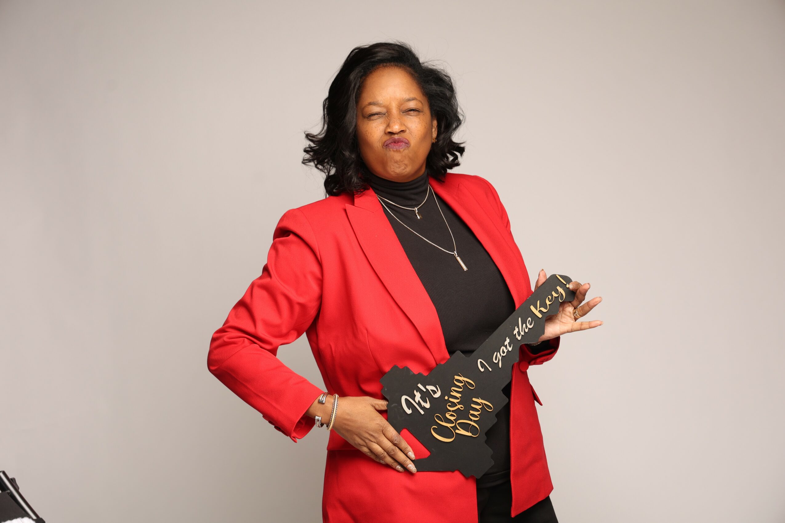 Woman in red blazer holding a sign, standing against a plain background.