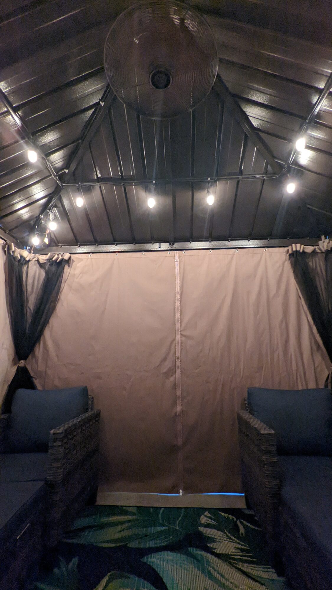 Indoor space with curtains, two chairs, and a ceiling with a large circular object and lights.