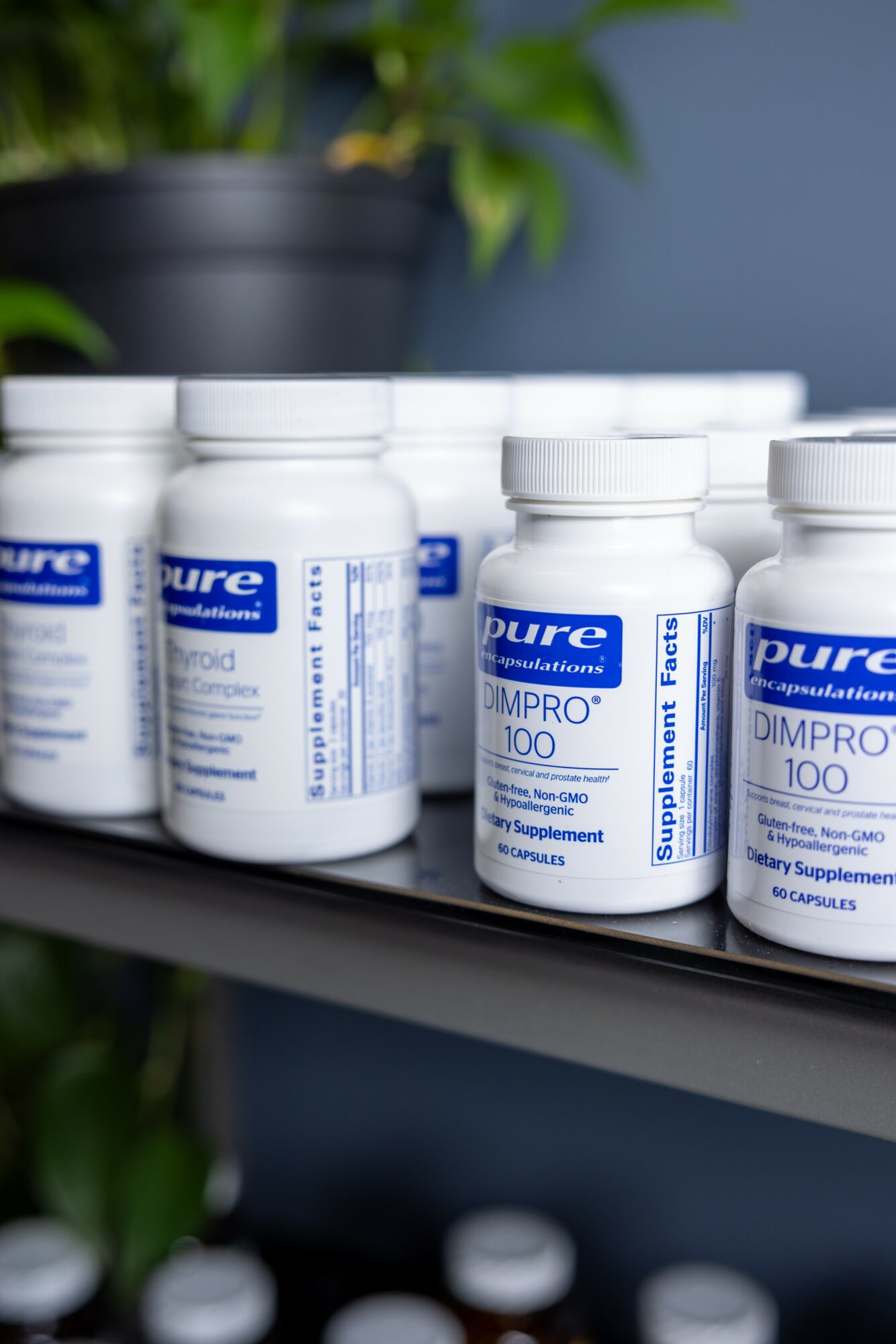 Bottles of dietary supplement labeled 'DIMPRO 100' on a shelf, with a plant in the background.