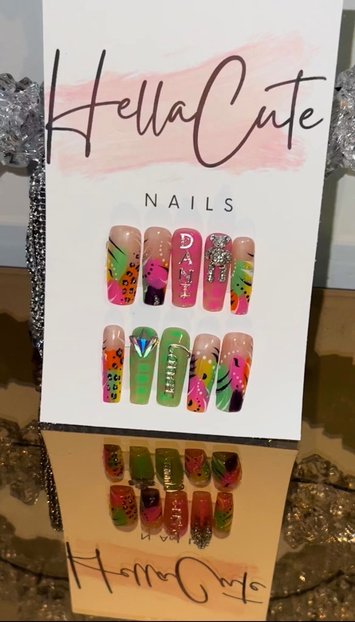 Display card with colorful nail designs and the text 'Hello Cute' in cursive, with a pink background. Word 'NAILS' below.