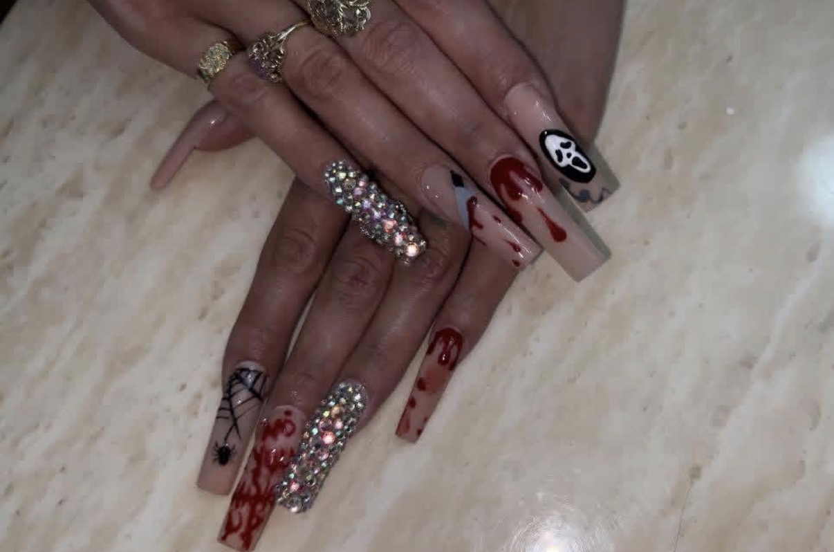 Hands with decorated nails, some with red and black designs, and wearing multiple rings, resting on a light surface.