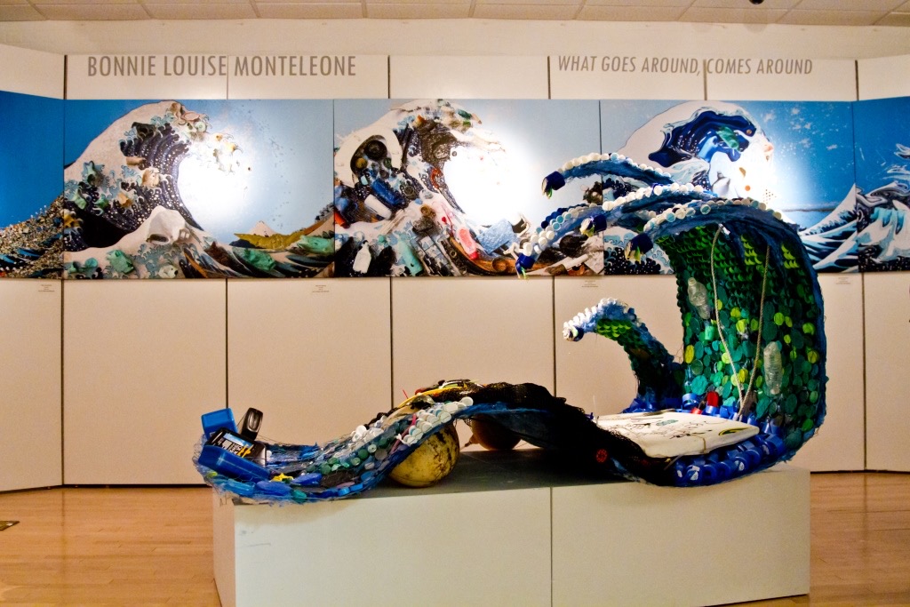 Mixed media artwork depicting ocean waves and a large fish, with text at the top reading 'Bonnie Louise Monteleone' and 'What Goes Around Comes Around'.
