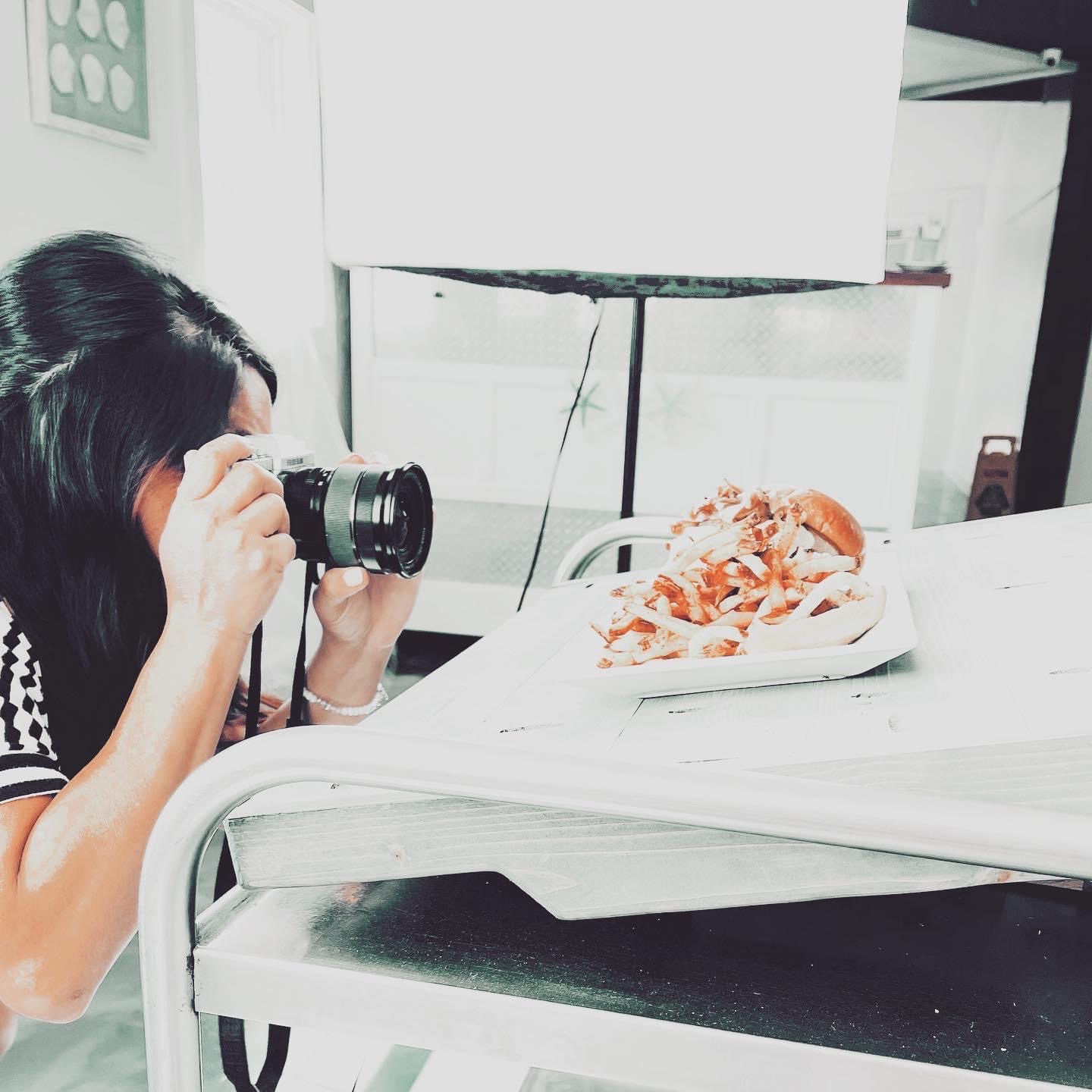 Person taking a photo of a plate of food on a table in a bright room.