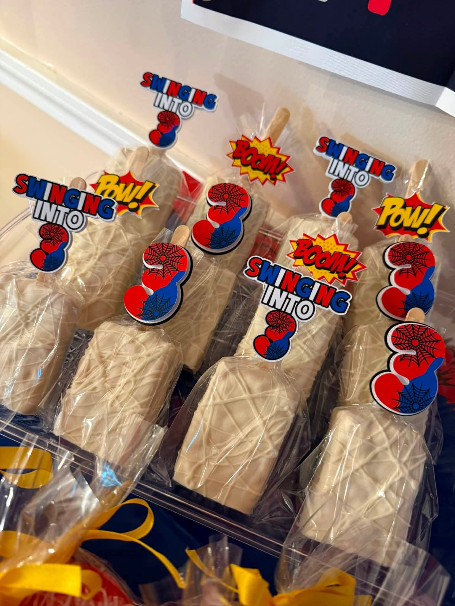 Party favors with Spider-Man themed decorations, including comic-style words like 'POW!' and 'BAM!', arranged on a table.