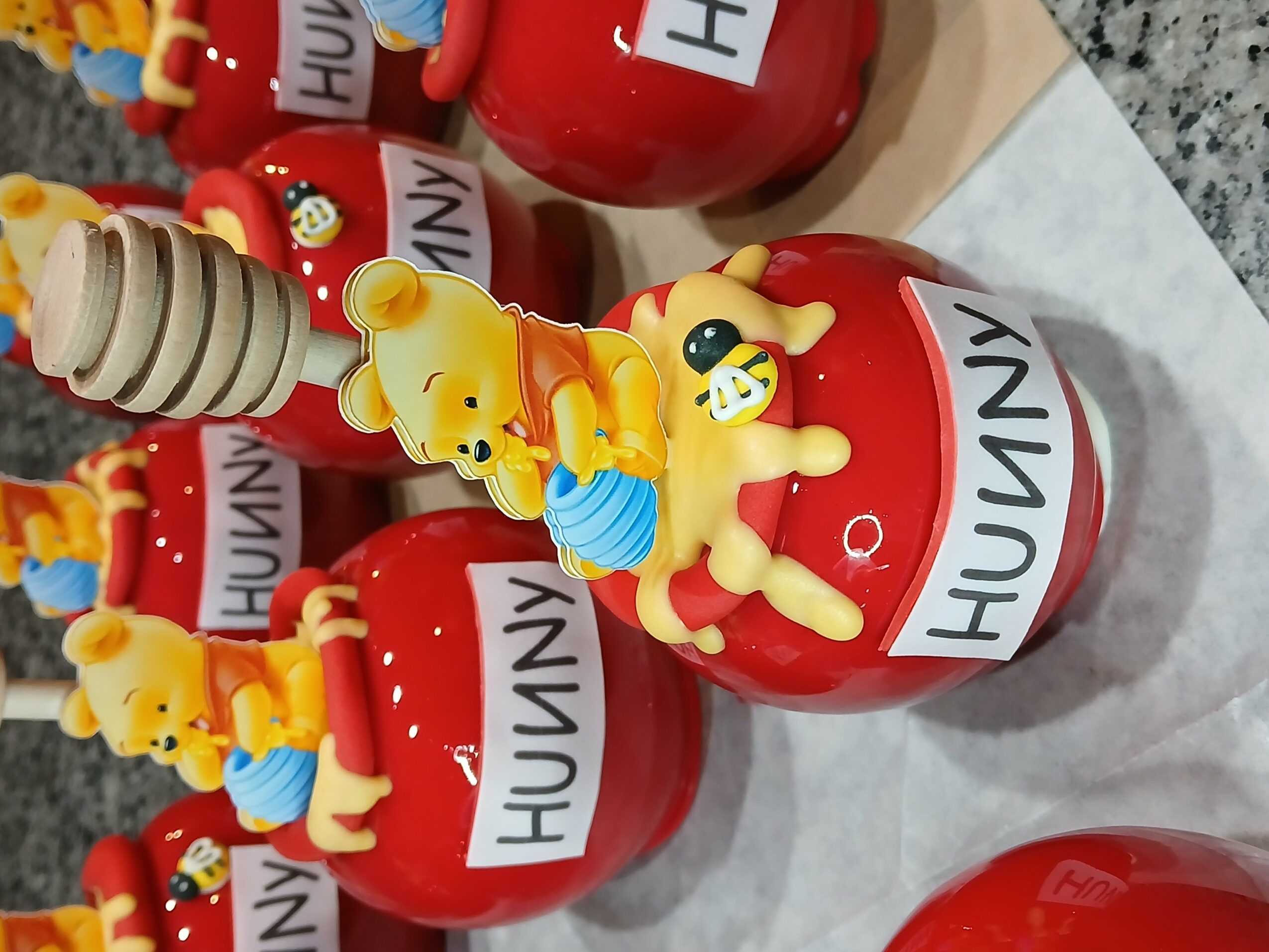 Red apple-shaped container with a yellow duck figurine holding a blue umbrella, labeled 'HUNNY', on a white surface.