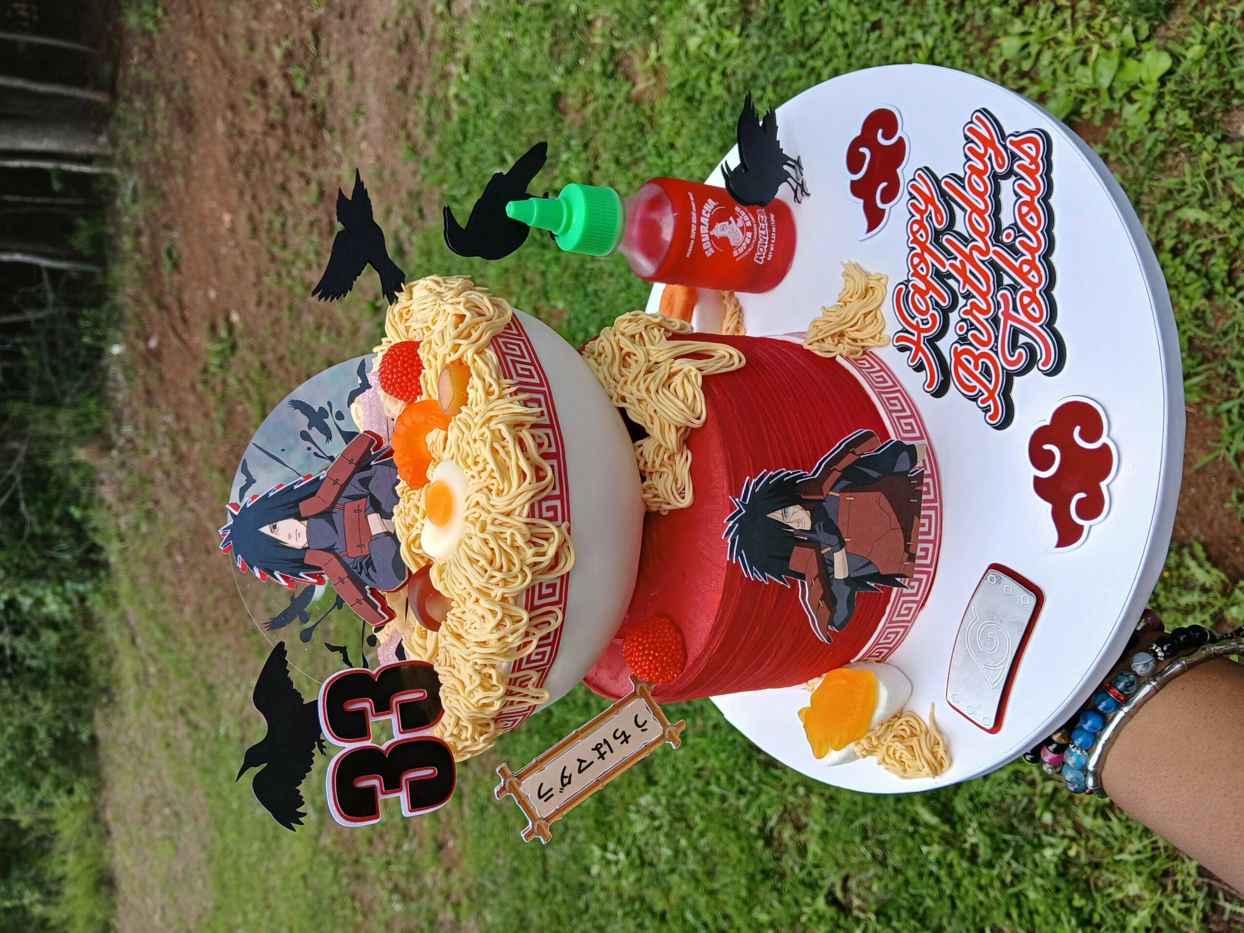Birthday cake with a 'Paw Patrol' theme, decorated with a character cutout, surrounded by toys and a bottle, outdoors.