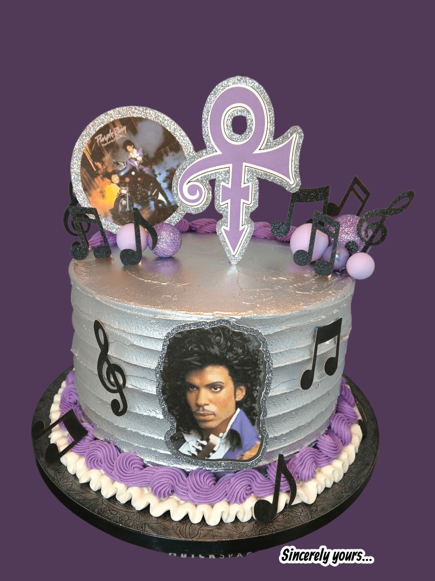 Decorated cake with musical notes, a portrait of Prince, and a purple symbol on top, against a purple background.