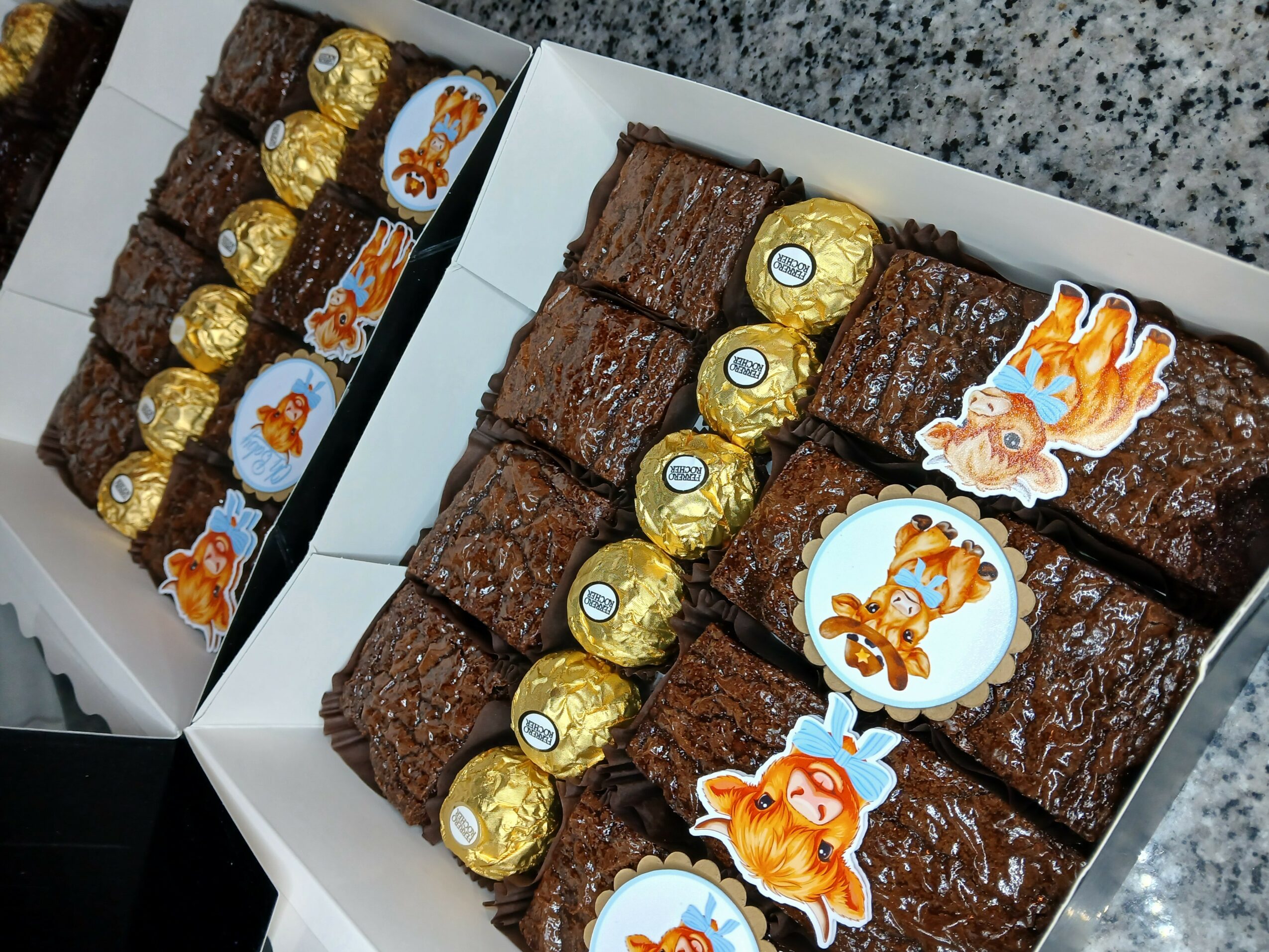Two open boxes of assorted chocolate treats on a gray surface, with various shapes and decorations, including gold-wrapped chocolates and animal stickers.