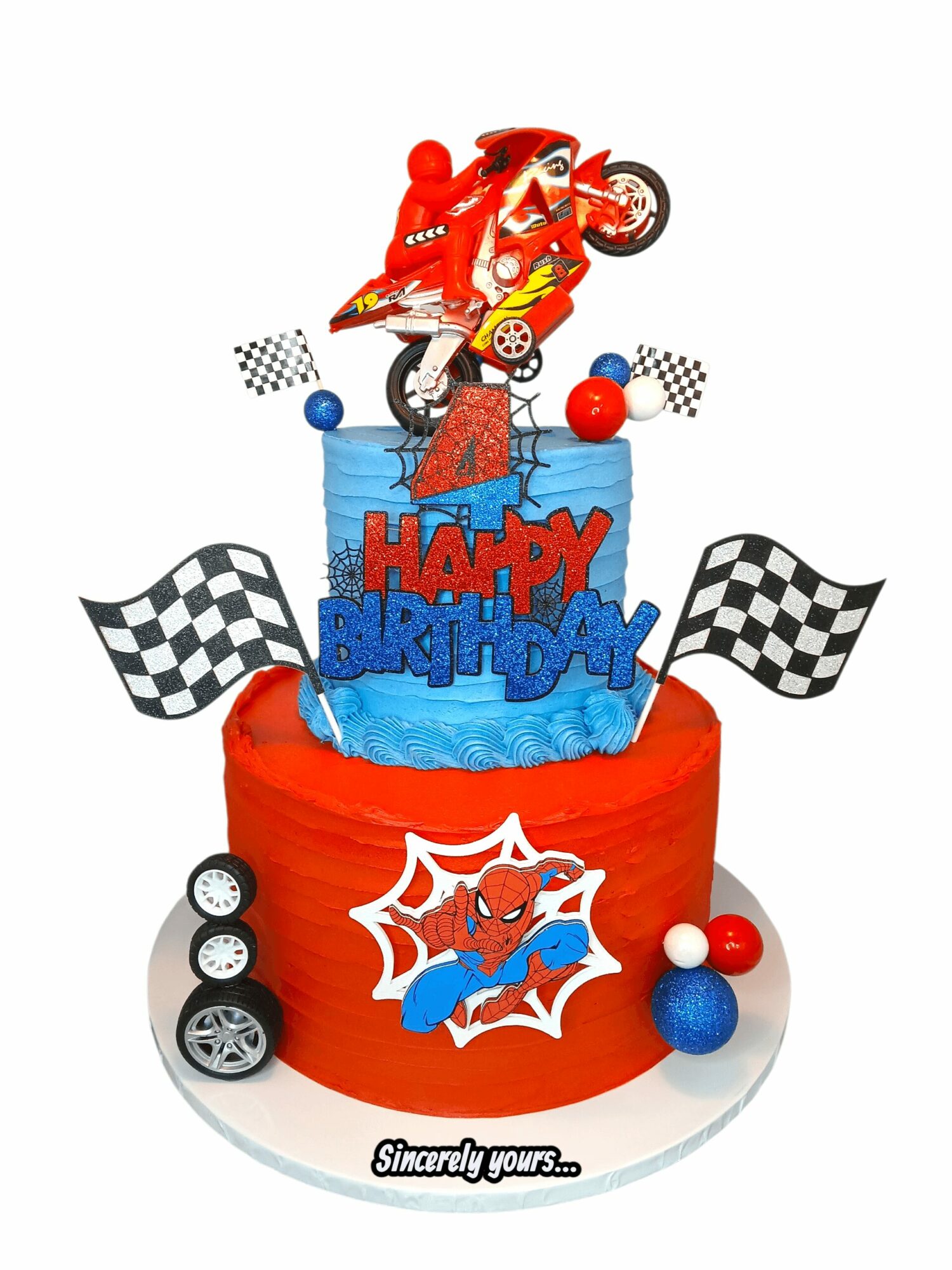 Two-tier birthday cake with racing car and checkered flag decorations, featuring a cartoon character and 'HAPPY BIRTHDAY' text, on a white background.