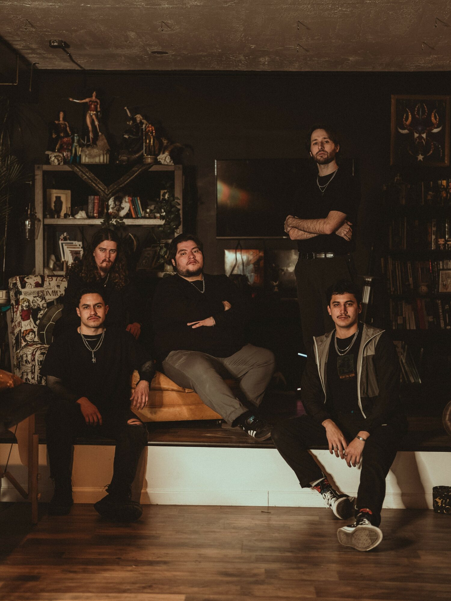 Five people in a room with shelves and a television, some sitting and one standing, in a casual setting.