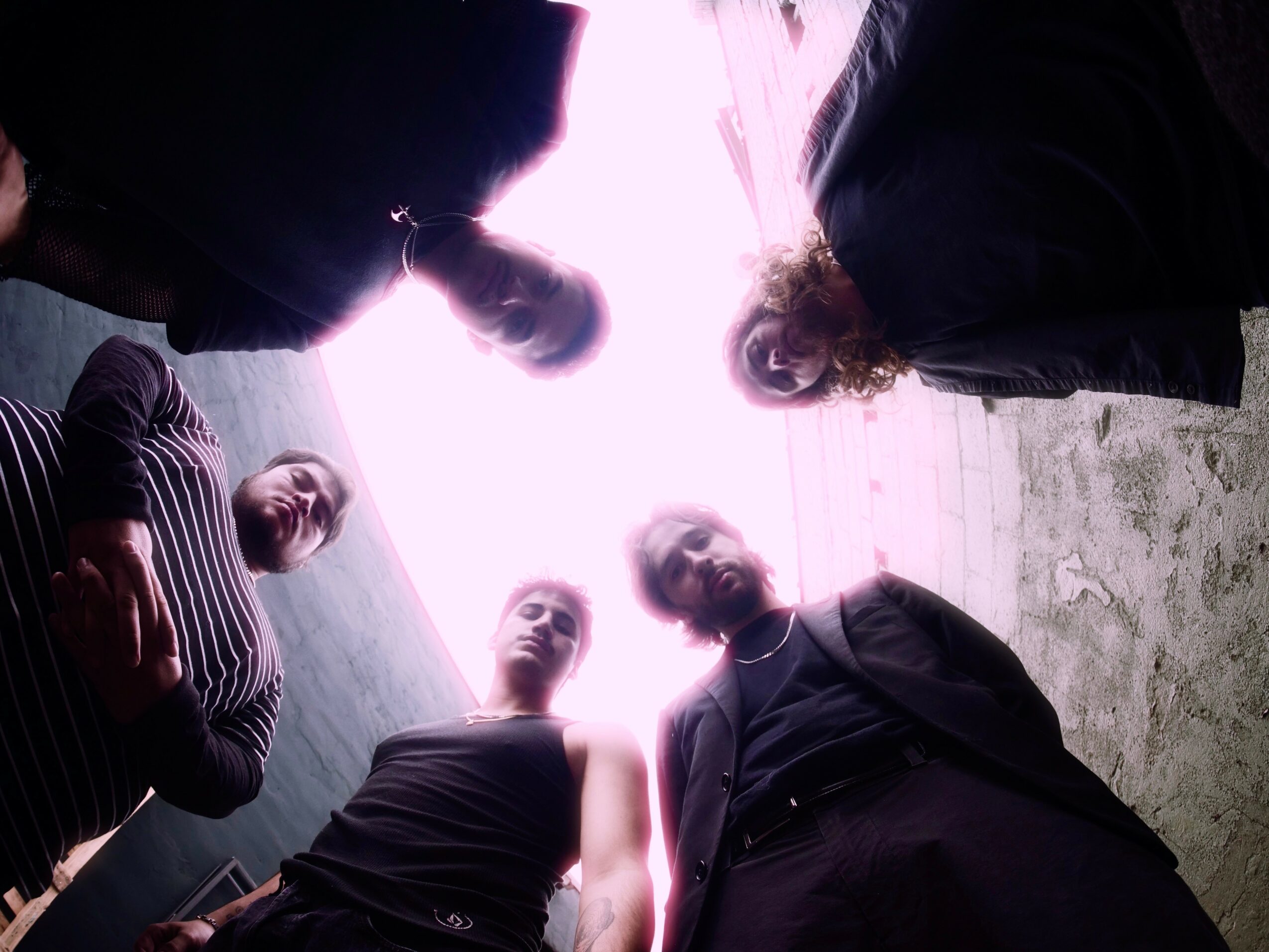 Group of people standing outdoors, viewed from below, with bright sky and clouds in background.