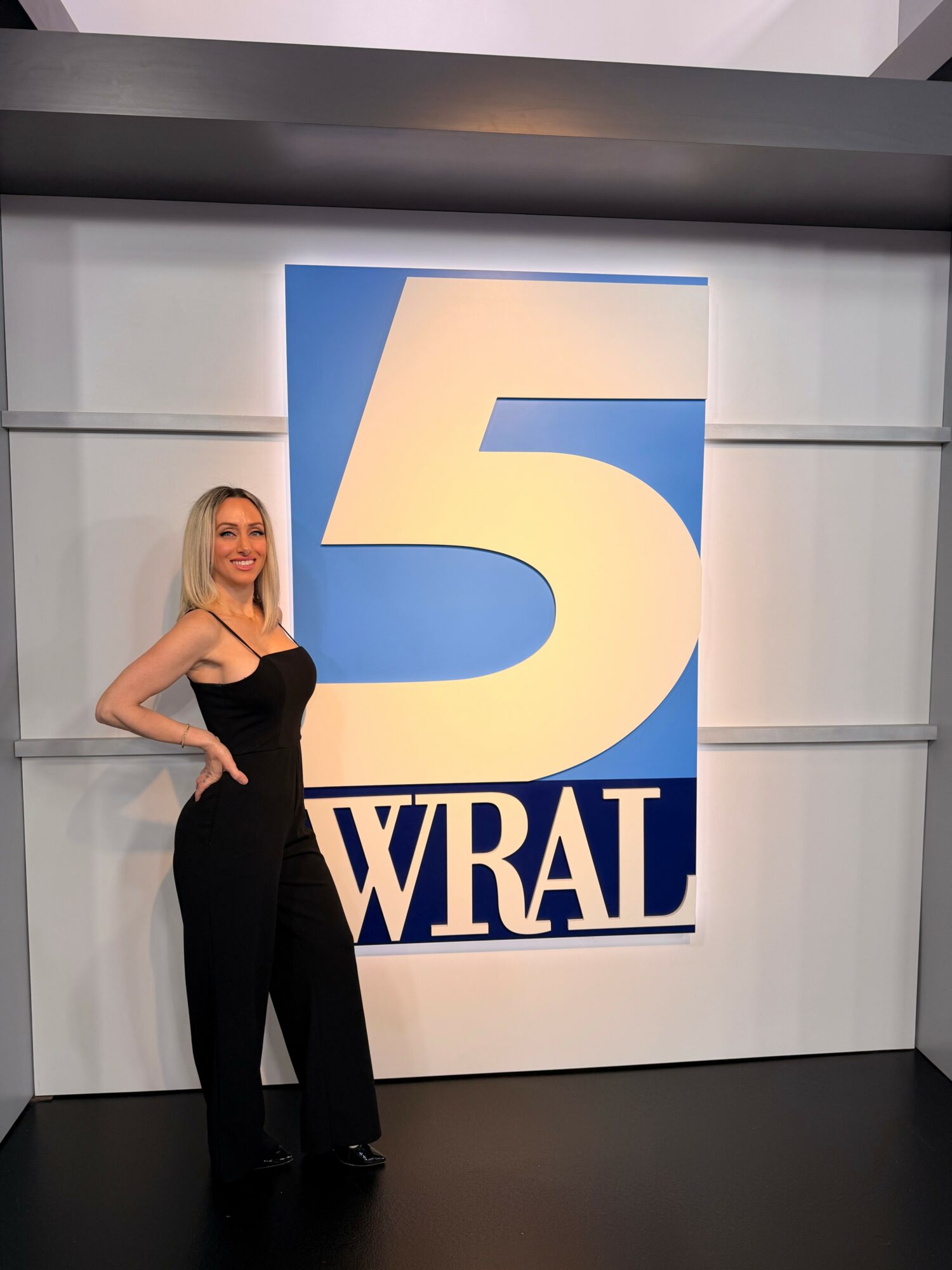 Woman in black outfit standing next to a large WRAL logo on a wall.