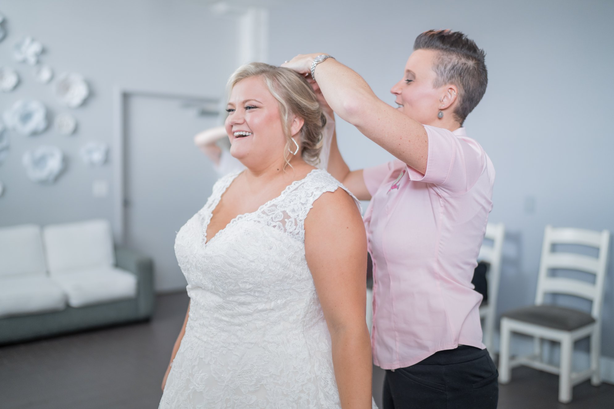 Person styling a woman's hair in a bright, modern room with white furniture and wall decorations.
