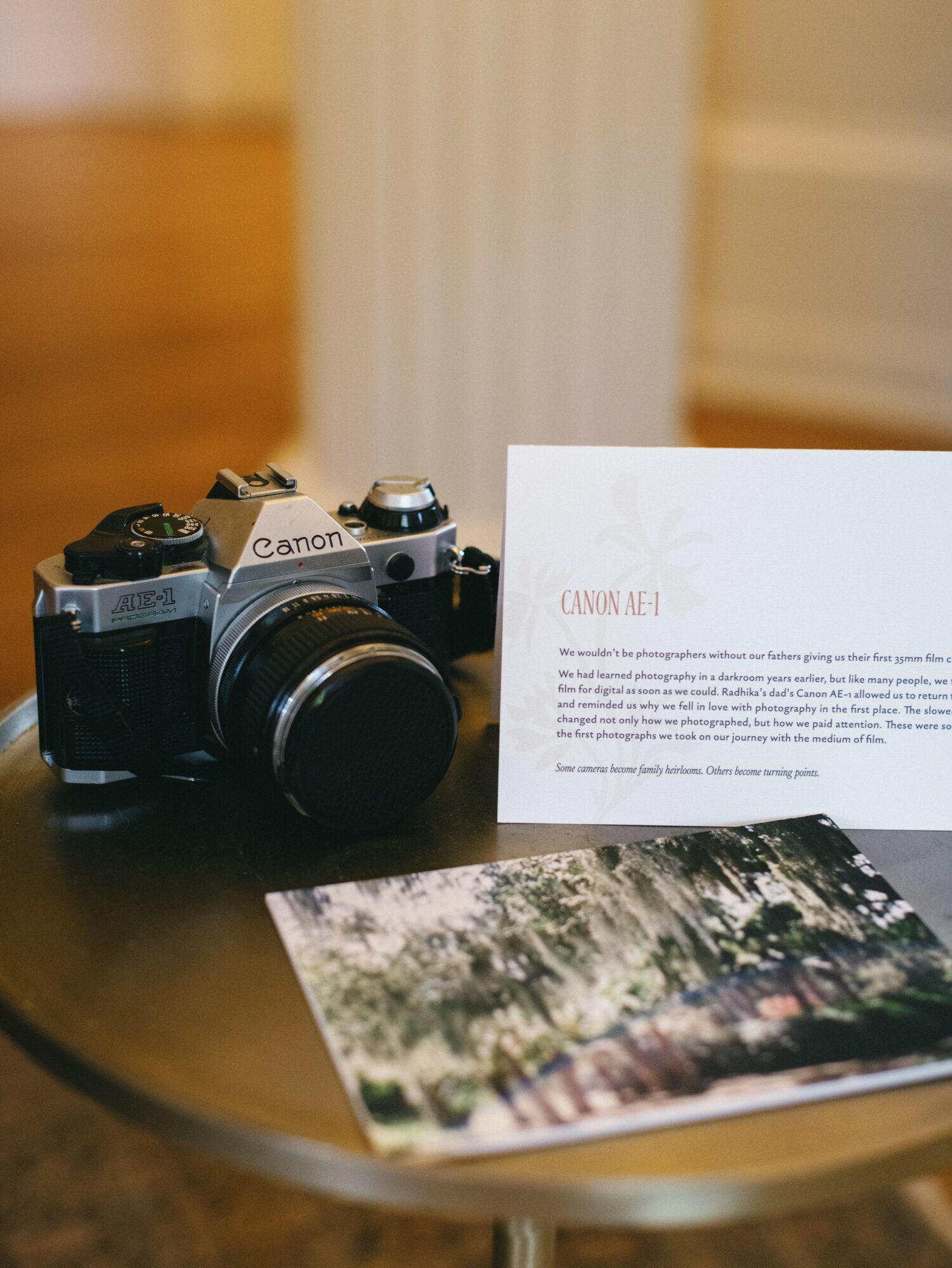 Canon AE-1 camera on a table with a photo and a document, background blurred, indoor setting.