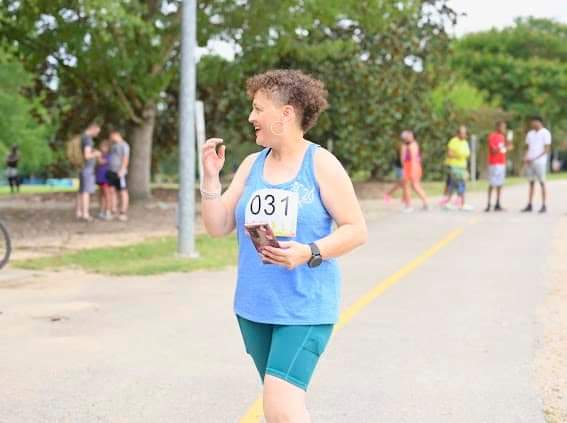 Young woman in blue athletic wear holding a race number and a photo, smiling during a race event outdoors.