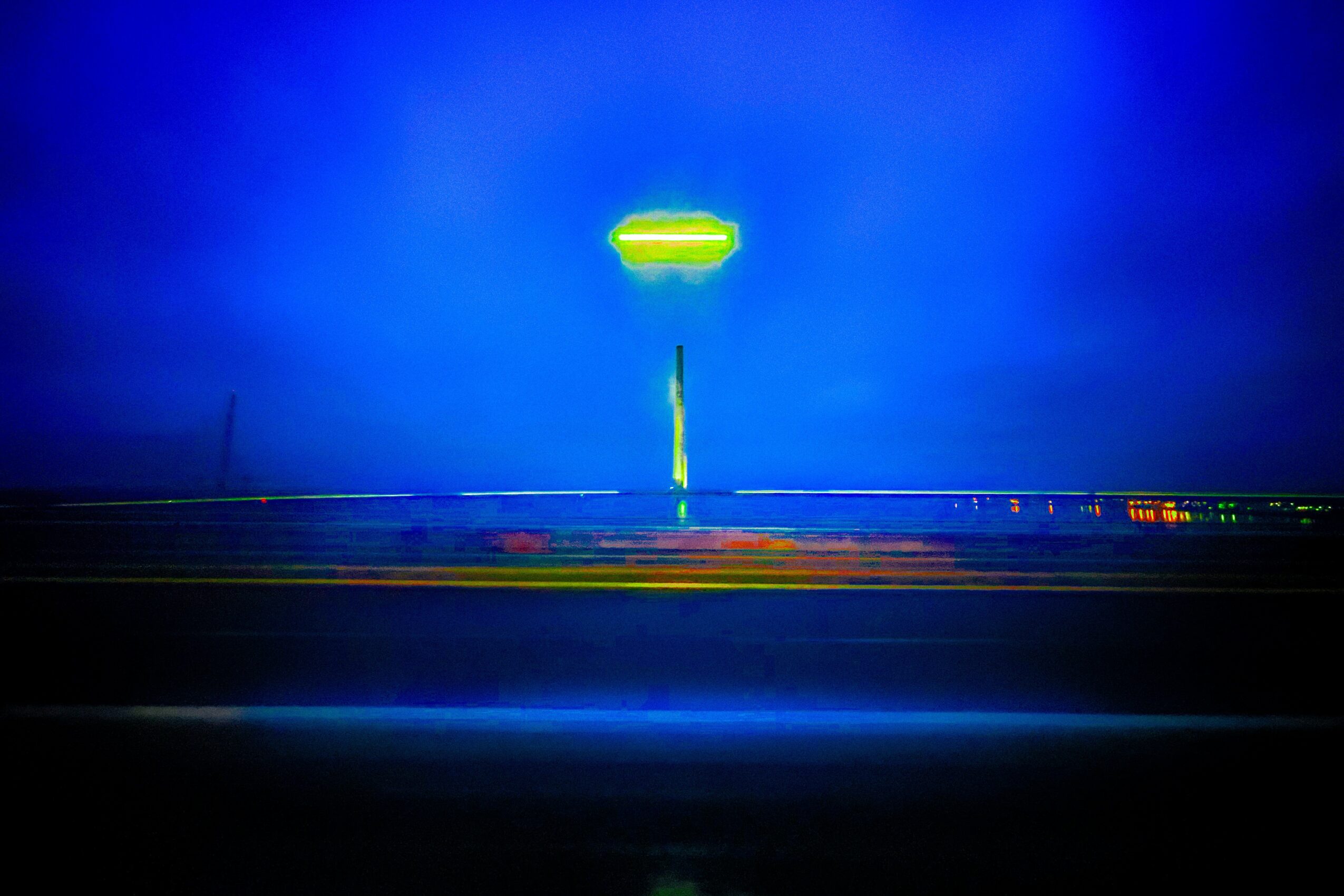 Bright yellow-green sign against a dark blue sky, with a road and horizon below, in a nighttime scene.