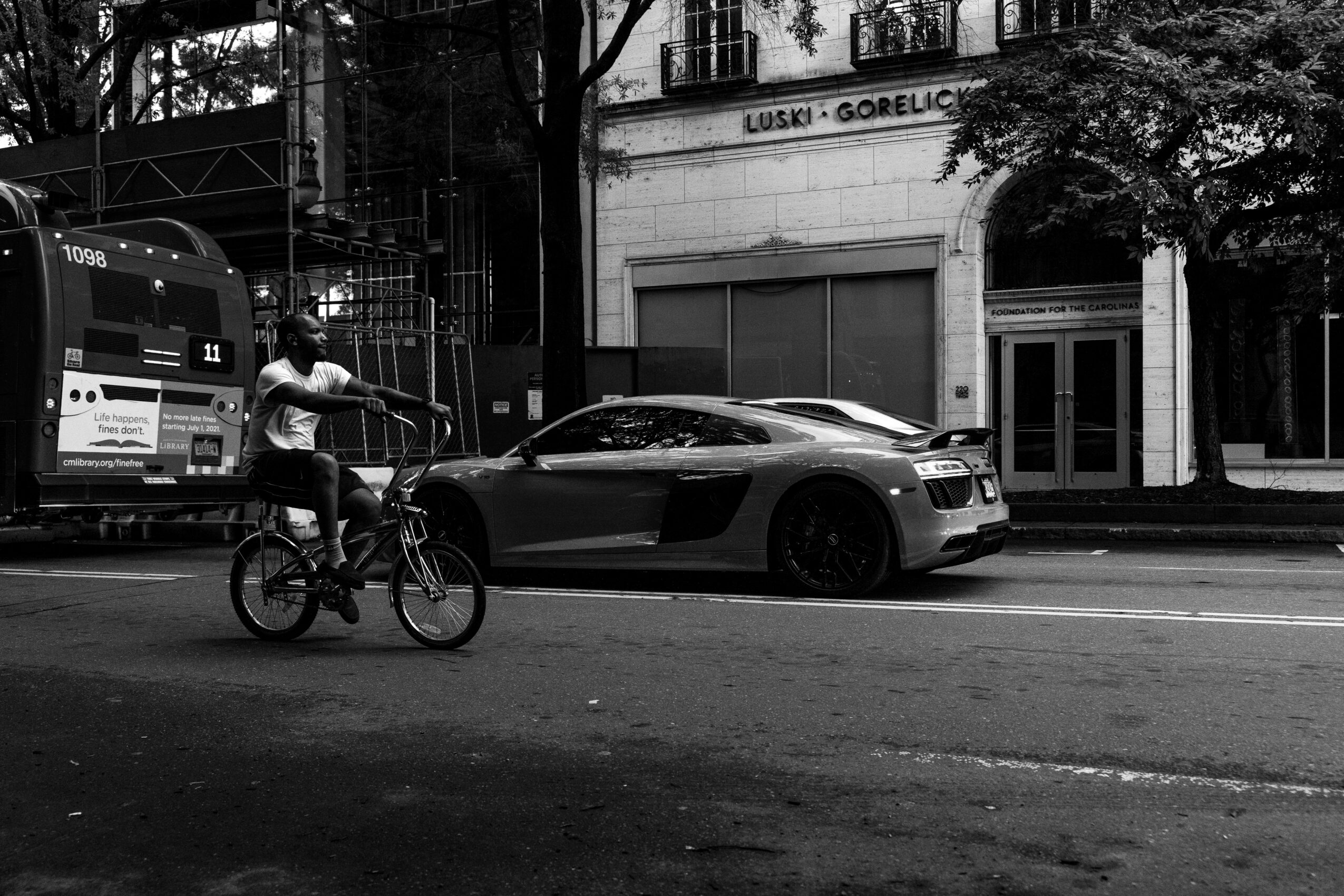 Person riding a bicycle on a city street with parked cars and buildings in the background.
