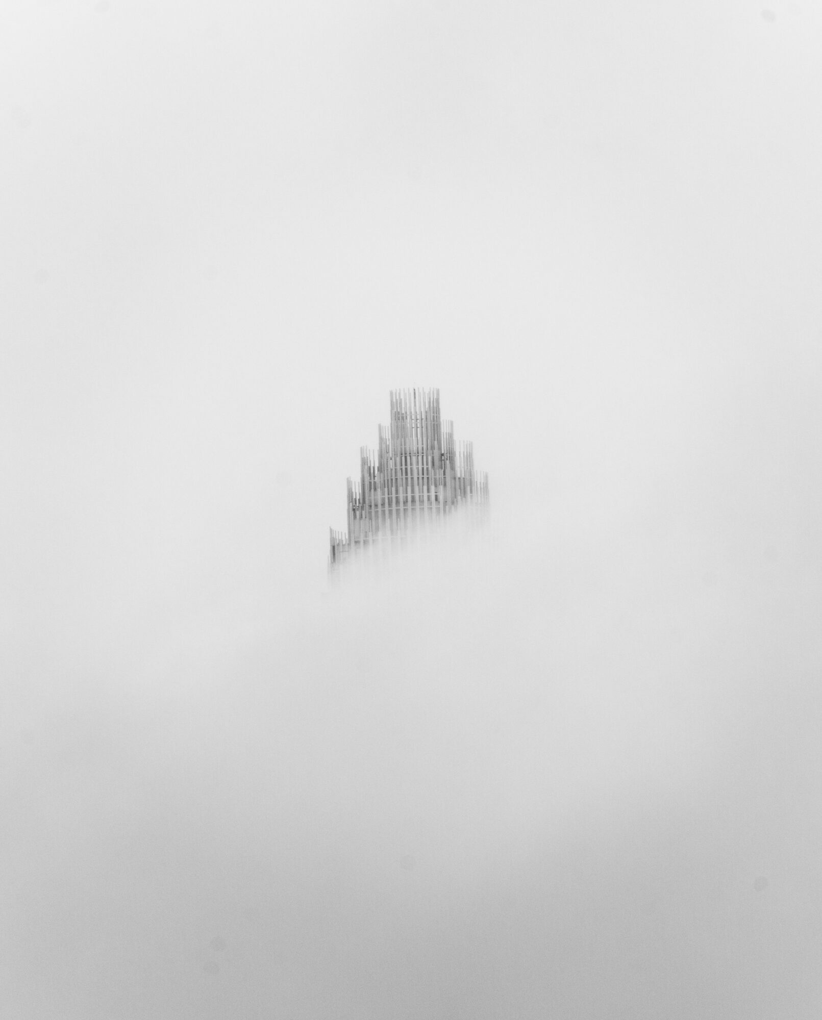 A tall building partially obscured by fog or clouds, with only the top visible.