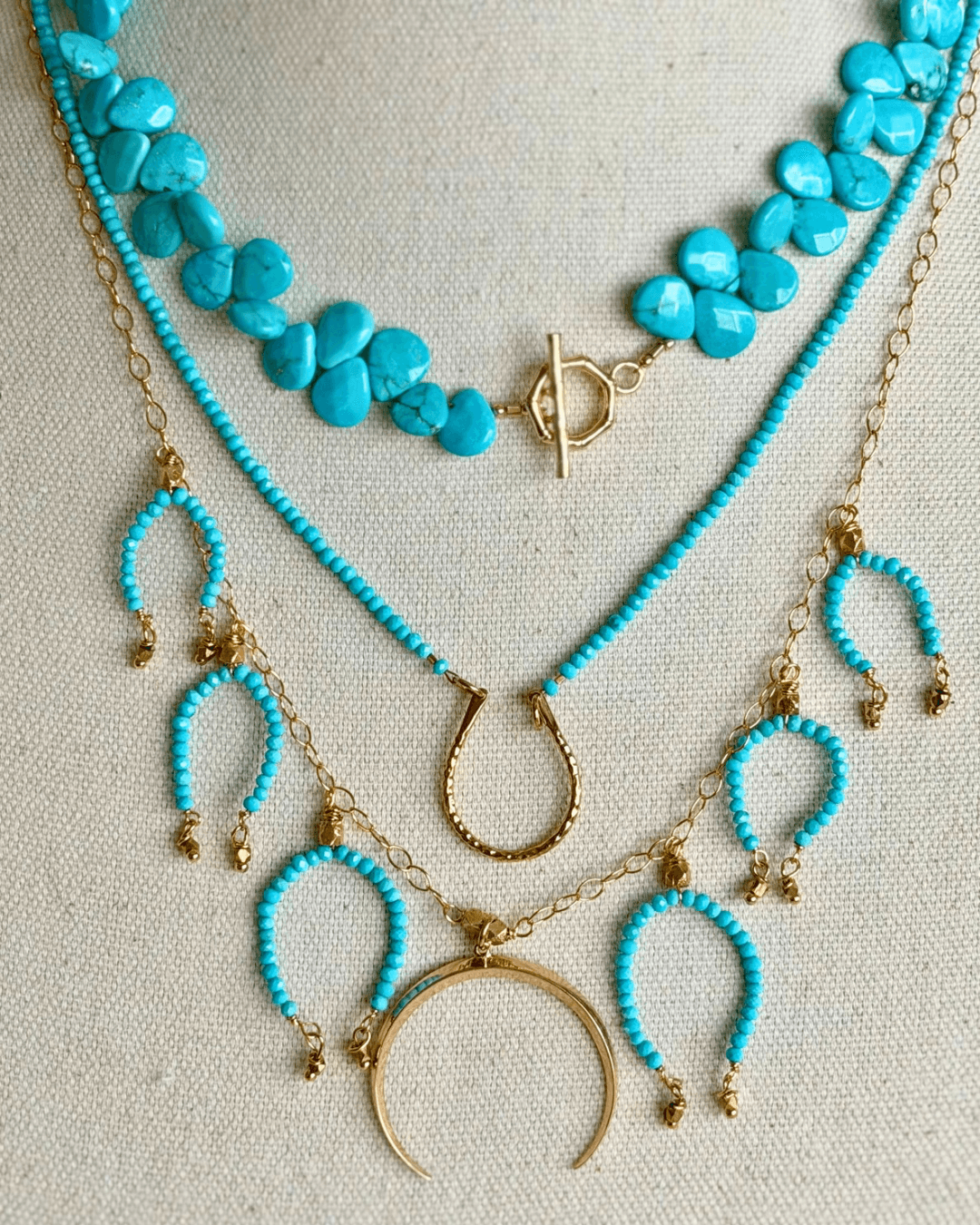 Three layered necklaces with turquoise beads and gold accents, including a crescent moon and horseshoe charms.