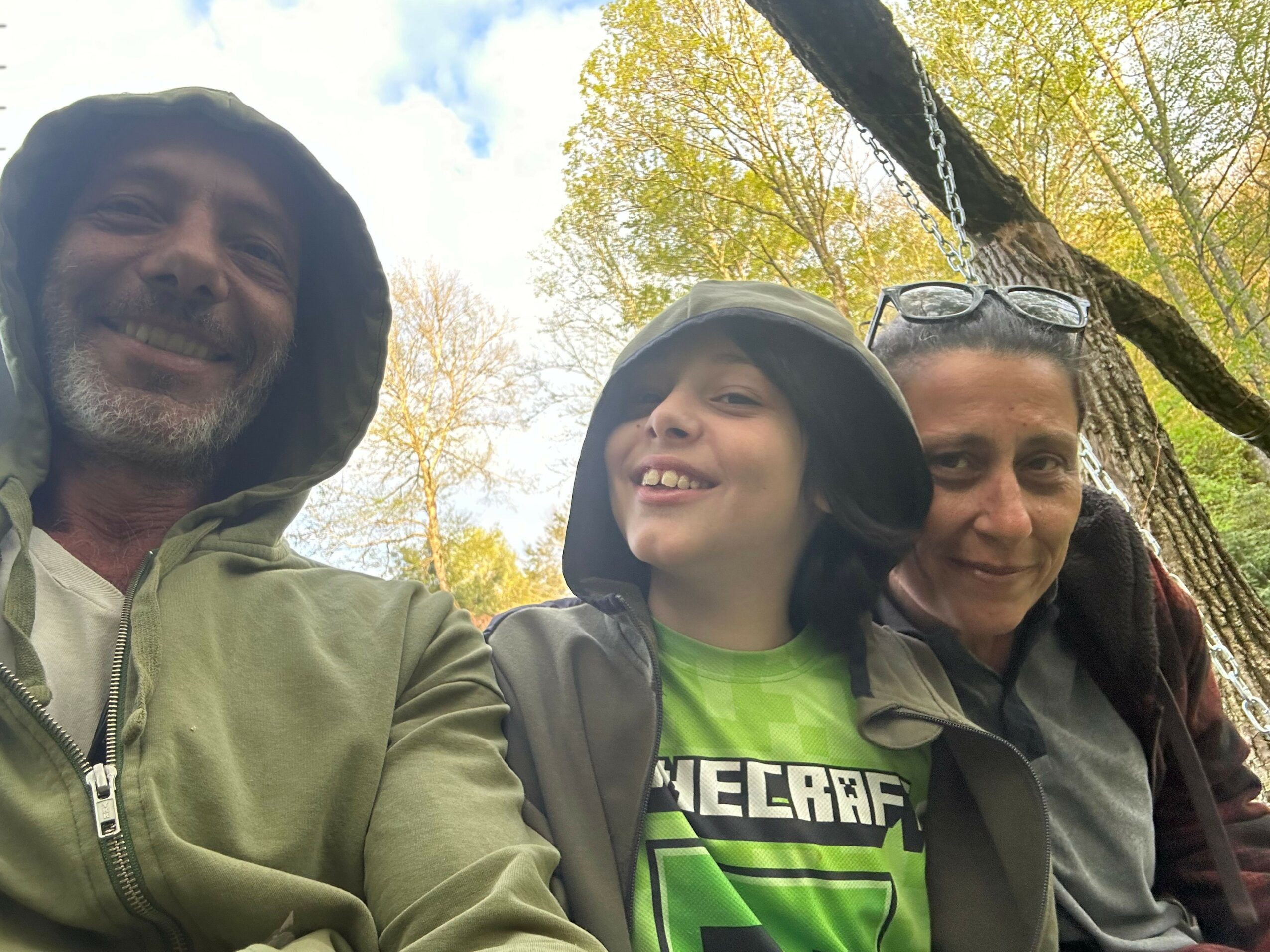 Three people outdoors, smiling, with trees and sky in the background.