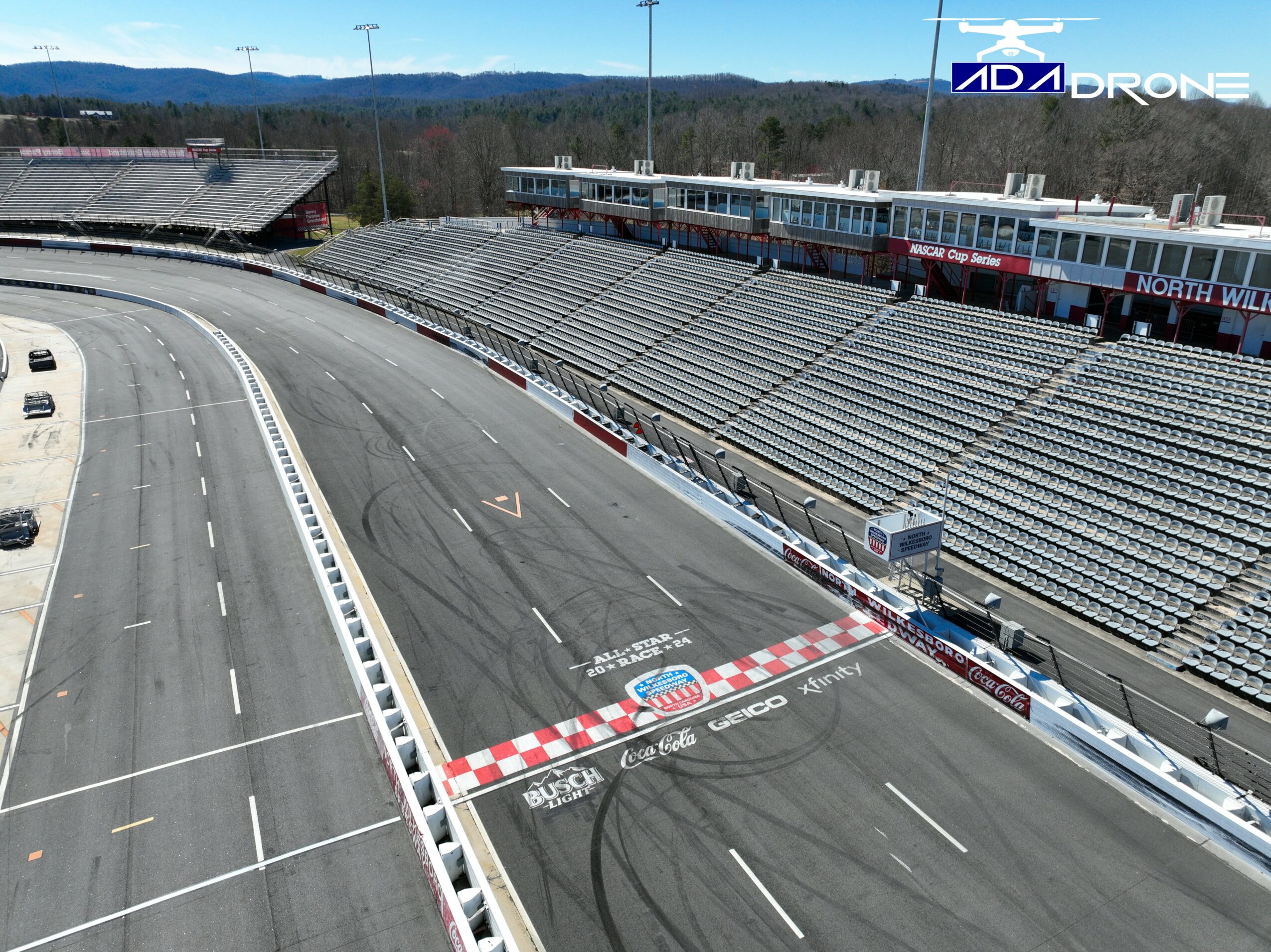 Empty race track with tire marks, surrounded by empty grandstands and a building in the background.