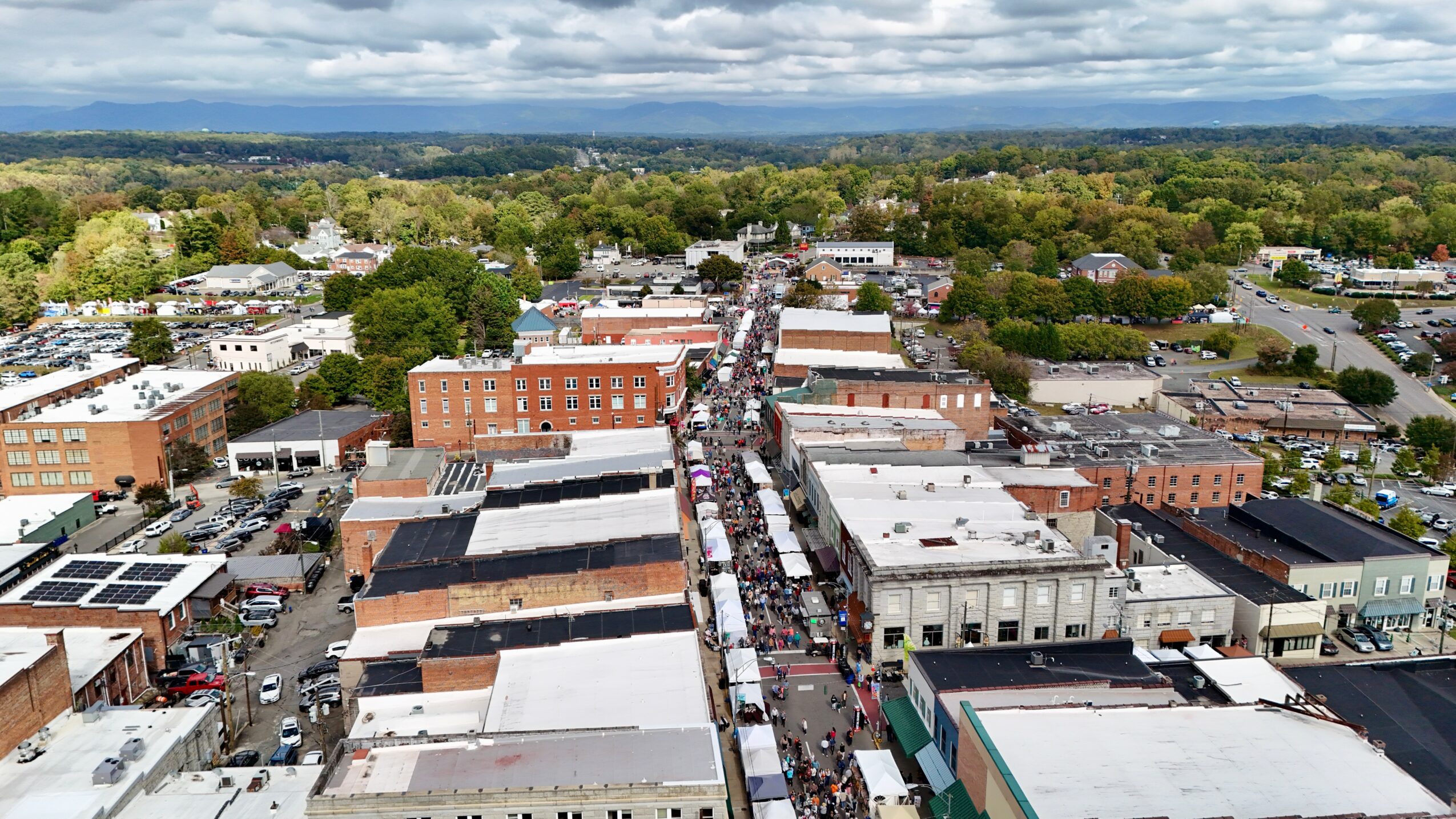 Aerial view of a small town with streets, buildings, and trees, extending into the distance under a cloudy sky.