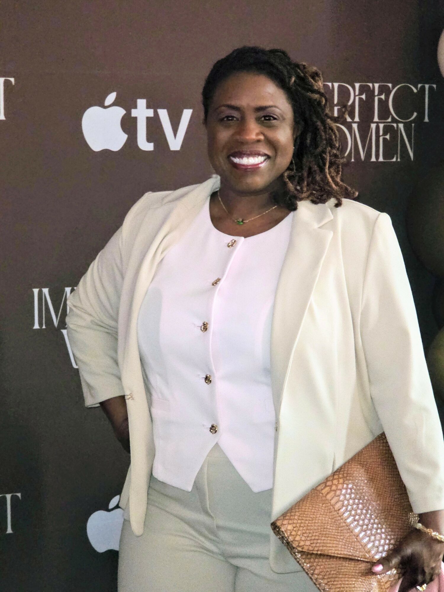 Woman smiling in white blazer and pants at an event with Apple TV and IMAX logos in background.