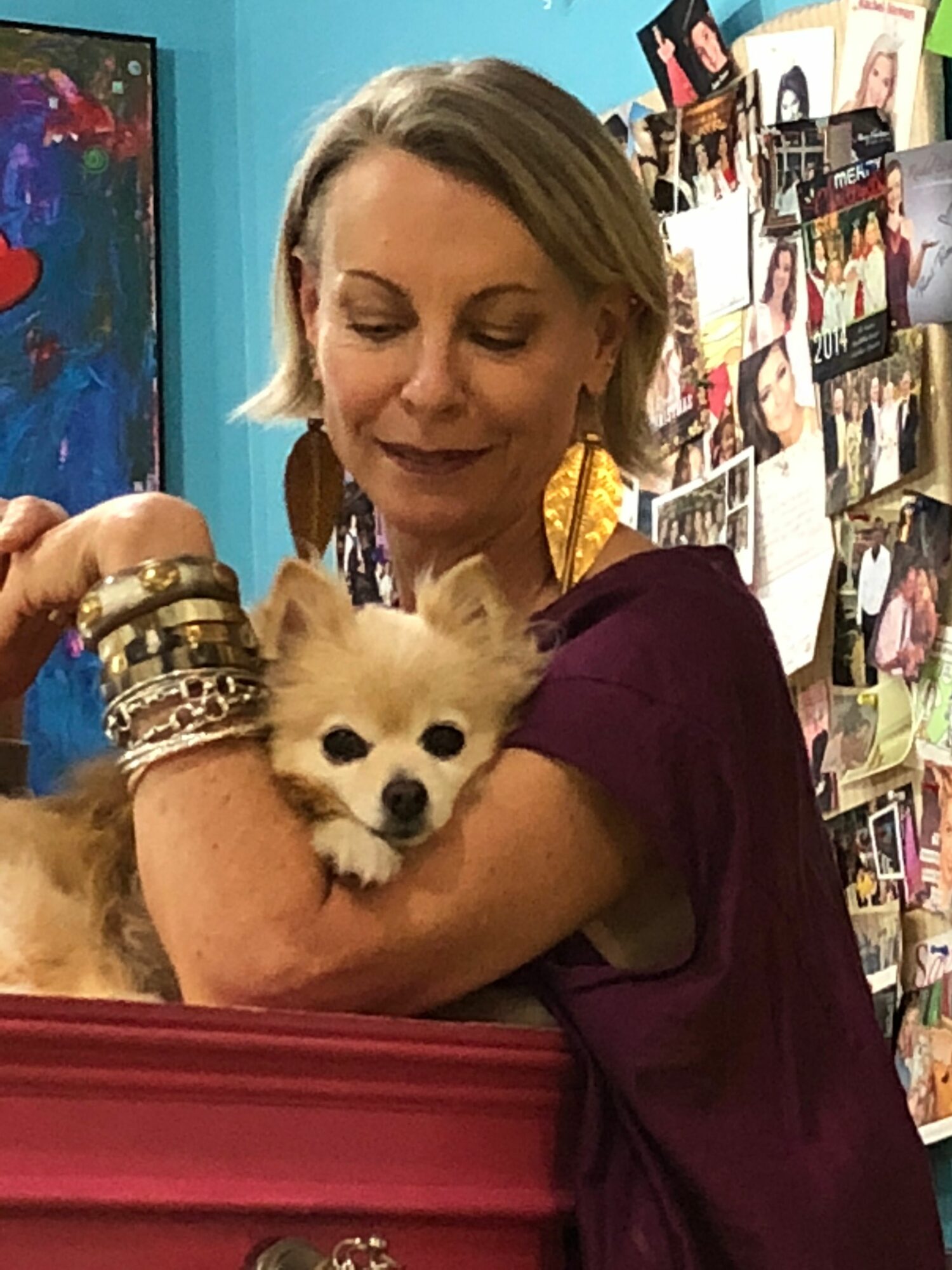Woman holding a small dog with a collage of photos in the background.