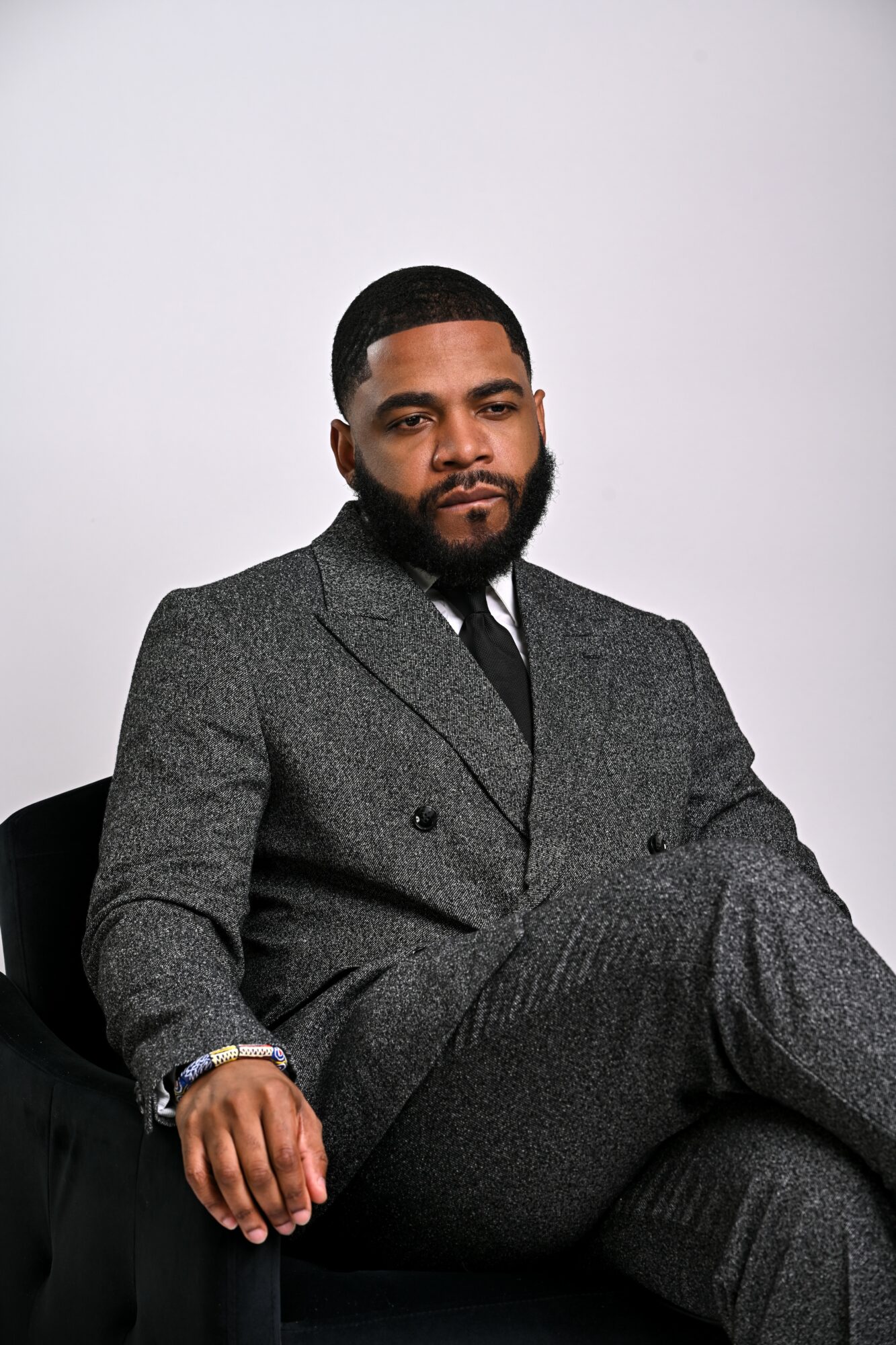 Man in a gray suit sitting with a serious expression, against a plain light background.